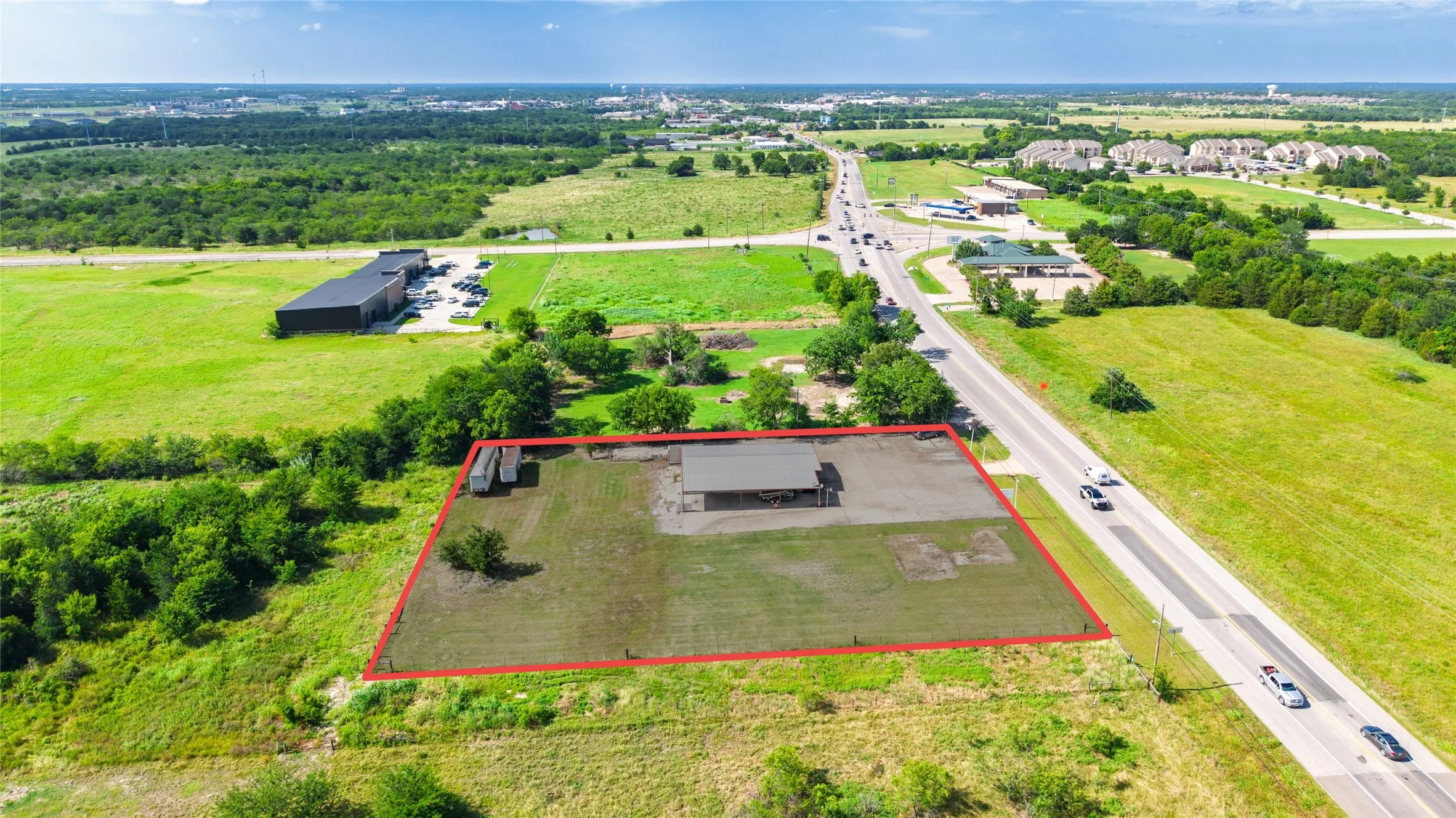 Aerial view showcasing a rectangular lot with a red boundary, featuring a small structure with a dark roof and a partial paved area