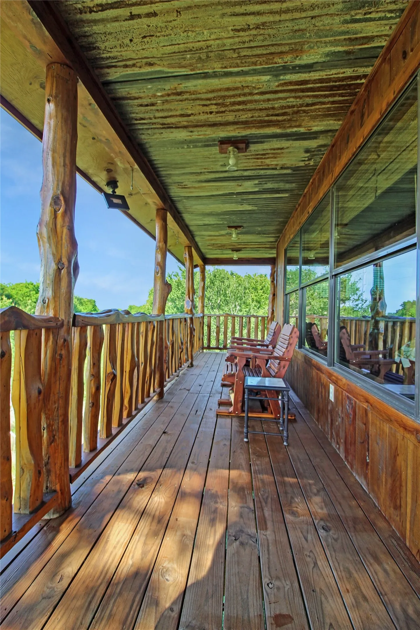 Expansive wood-plank porch featuring natural log posts, a rustic log railing, and a corrugated metal ceiling
