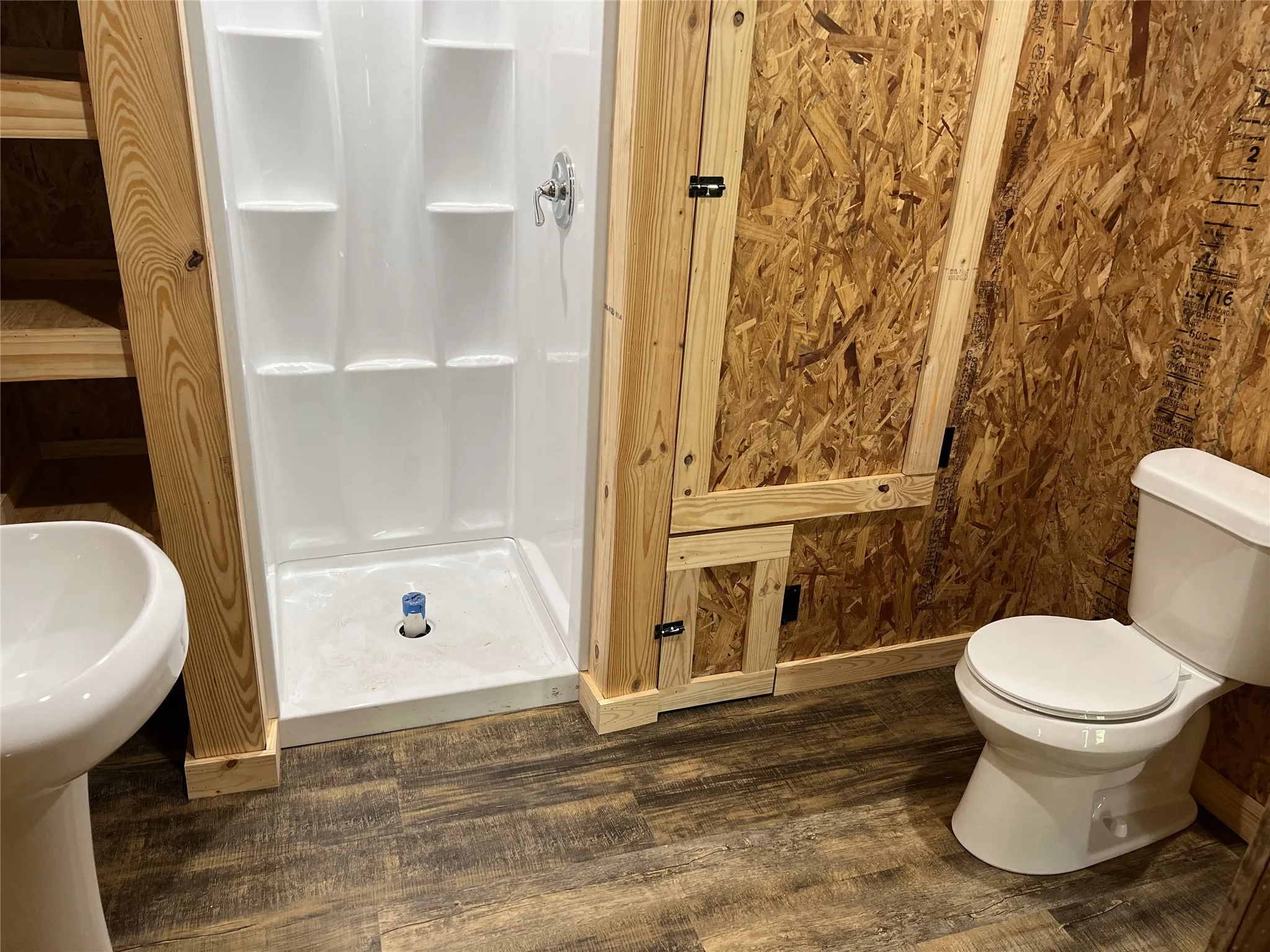 Compact bathroom featuring a white pedestal sink, a white toilet, and a white one-piece shower stall with chrome fixtures