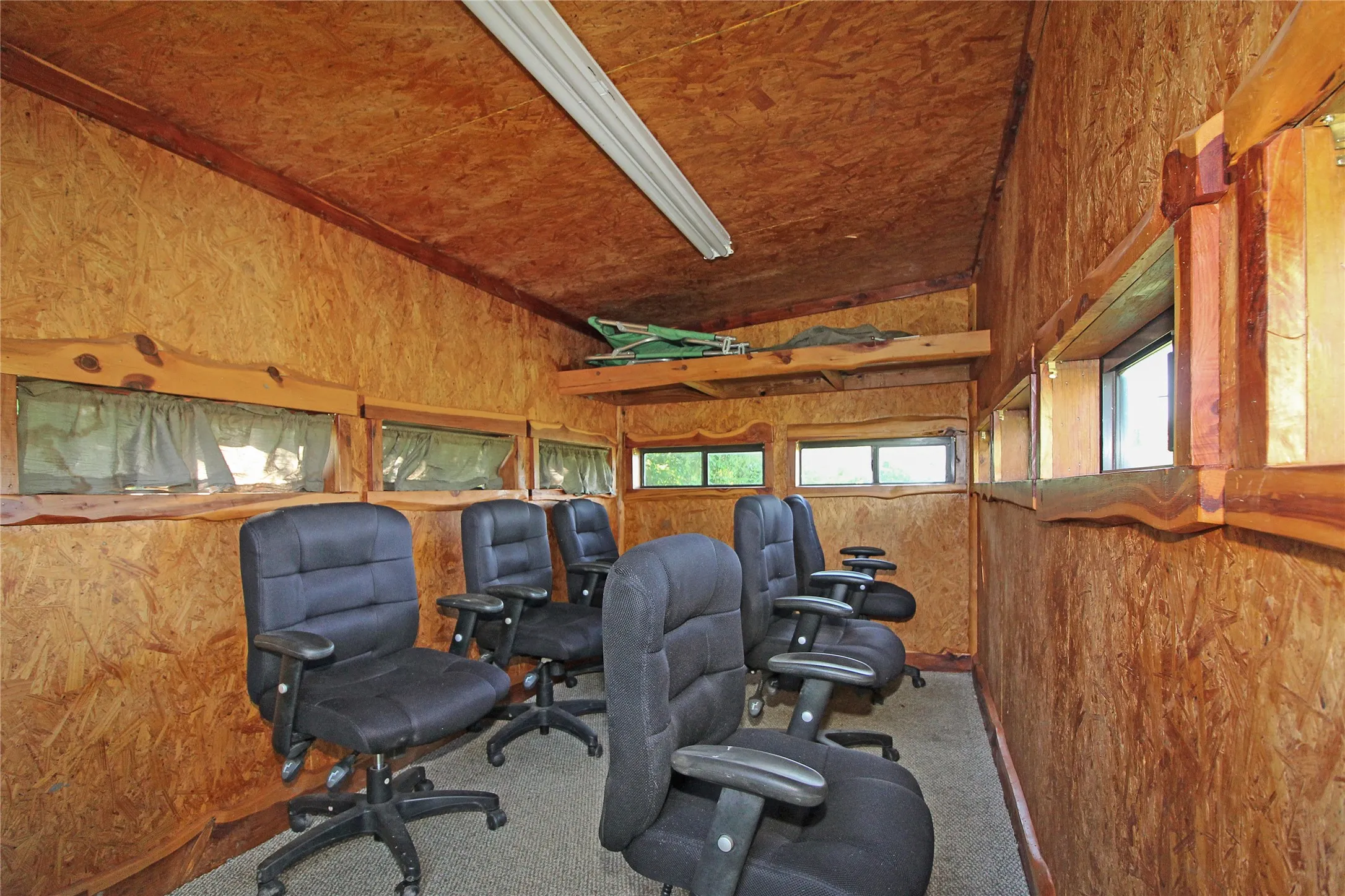 Interior space with oriented strand board walls and ceiling, featuring multiple horizontal windows with wood trim