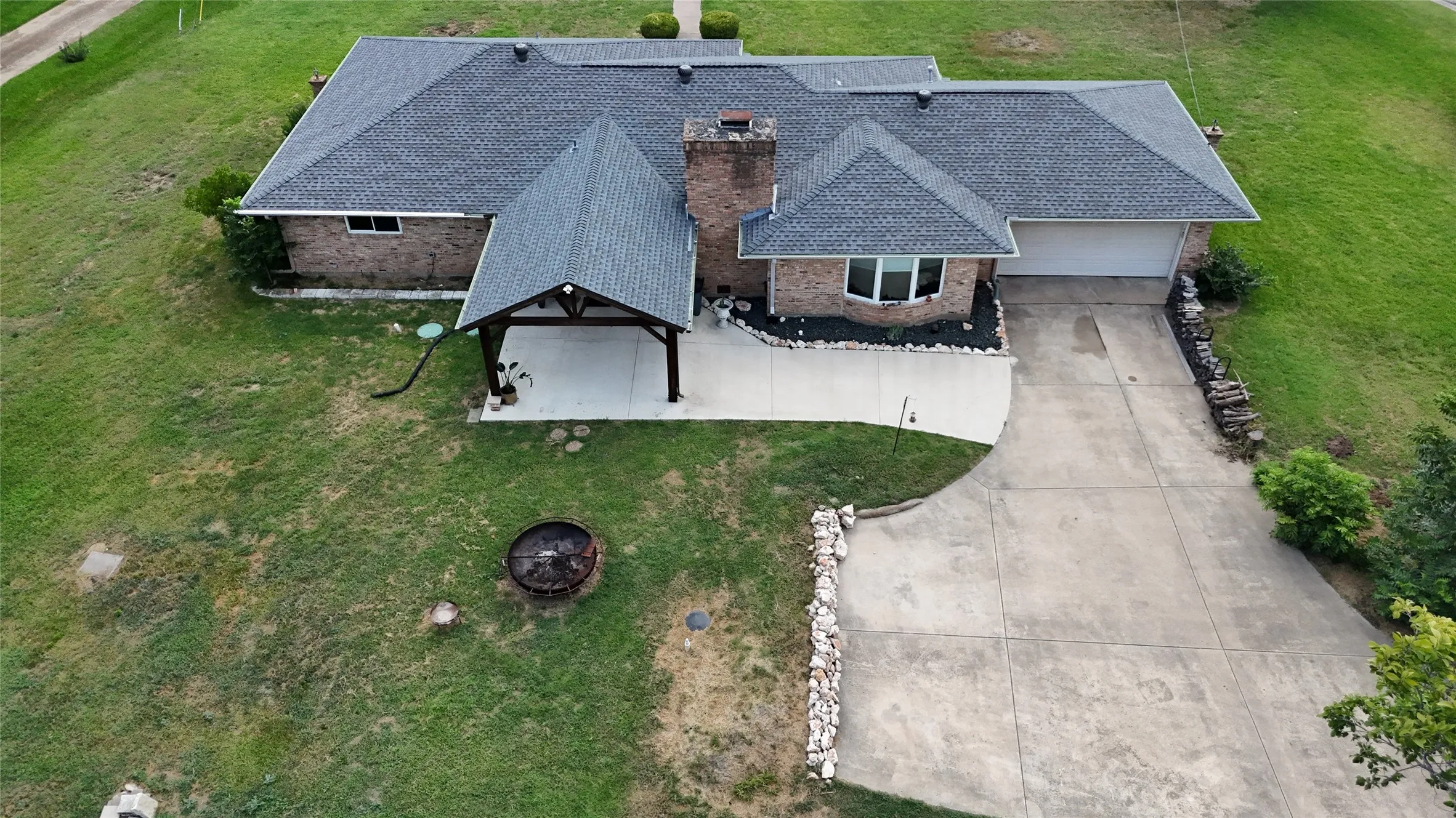 Brick exterior residence featuring a dark shingle roof, attached two-car garage, and a covered carport with exposed beams