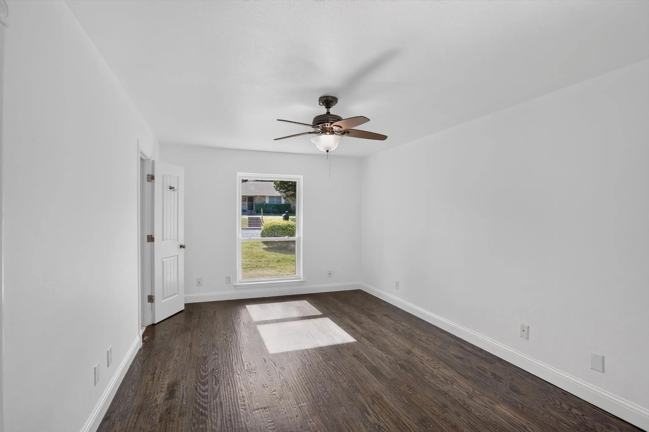 Bright room featuring dark wood-finish flooring, white baseboards, and a contemporary ceiling fan with integrated lighting