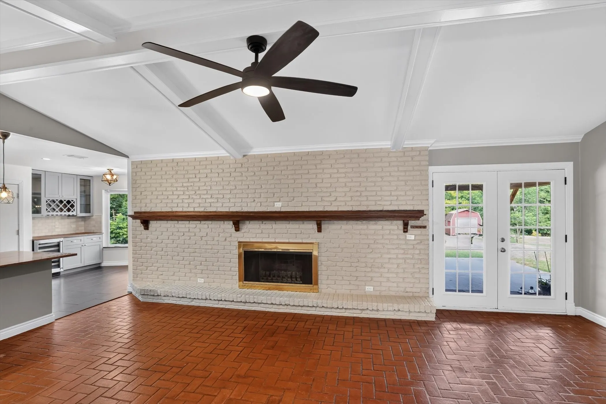 Vaulted ceiling with exposed beams, brick fireplace with wood mantel, herringbone brick flooring, and French doors
