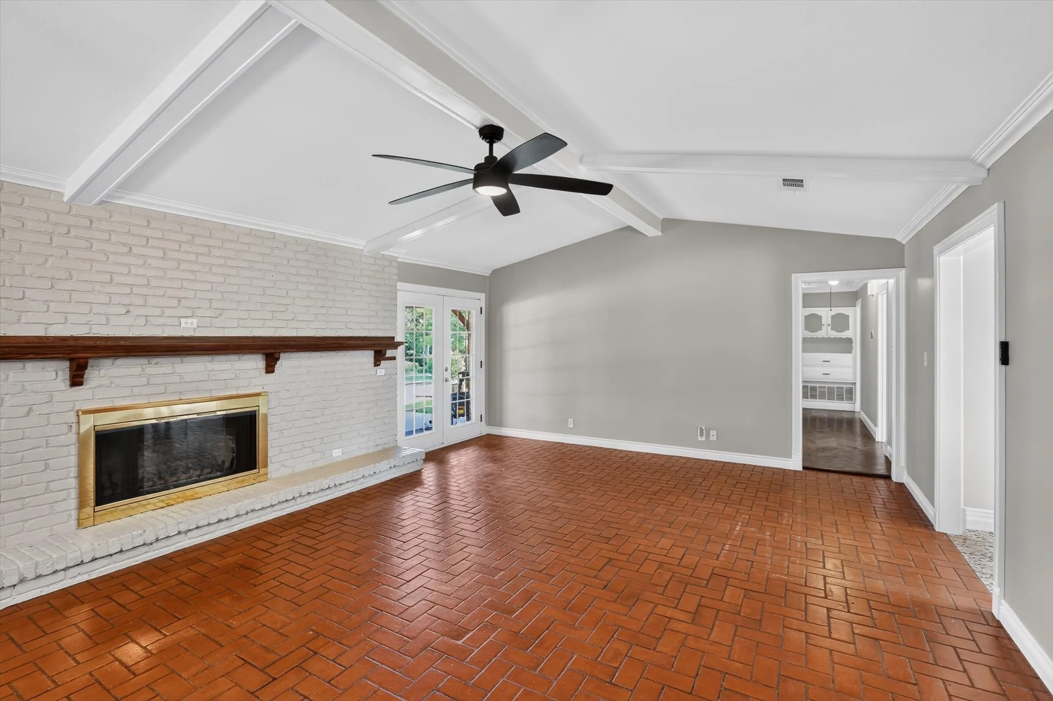 Spacious living area featuring exposed white ceiling beams, a painted brick fireplace with a wood mantle, and French doors