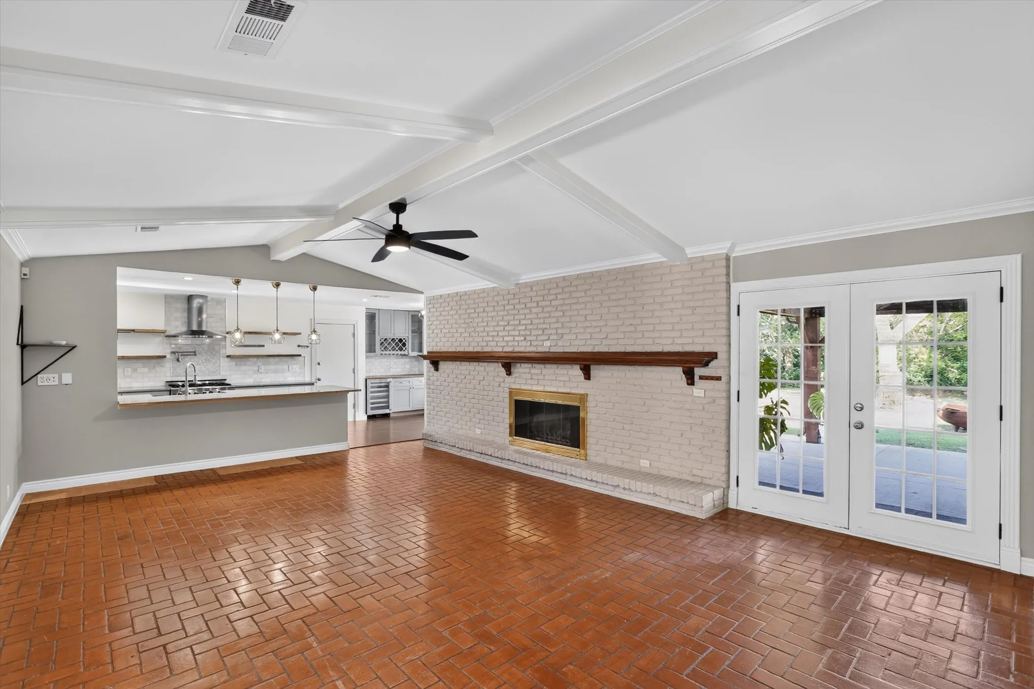 Spacious living area featuring brick-patterned flooring, a painted brick fireplace with a wood mantle, and bright French doors