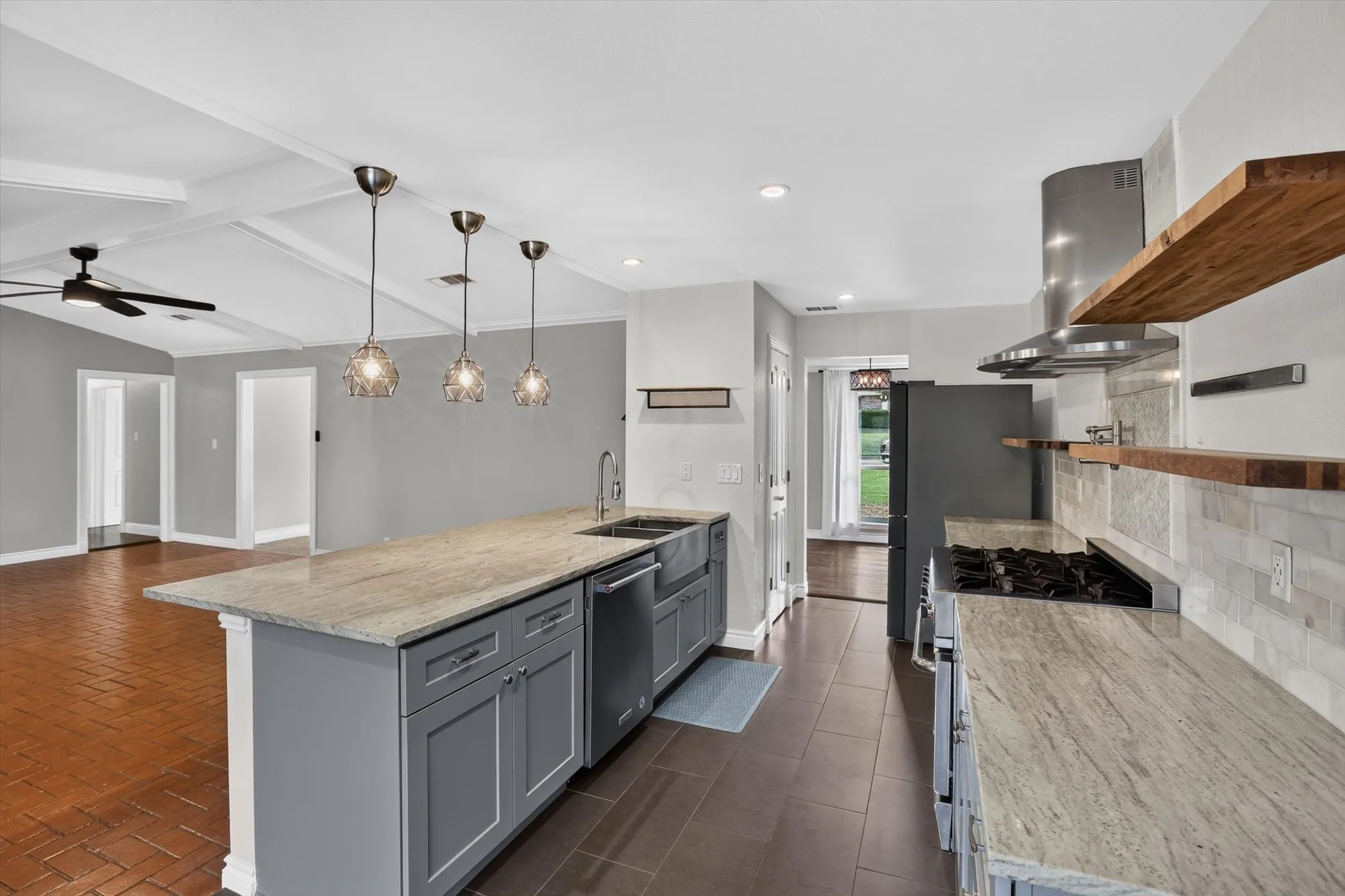 Kitchen featuring a center island with sink and pendant lighting, stainless steel appliances, open wood shelving, and tile flooring