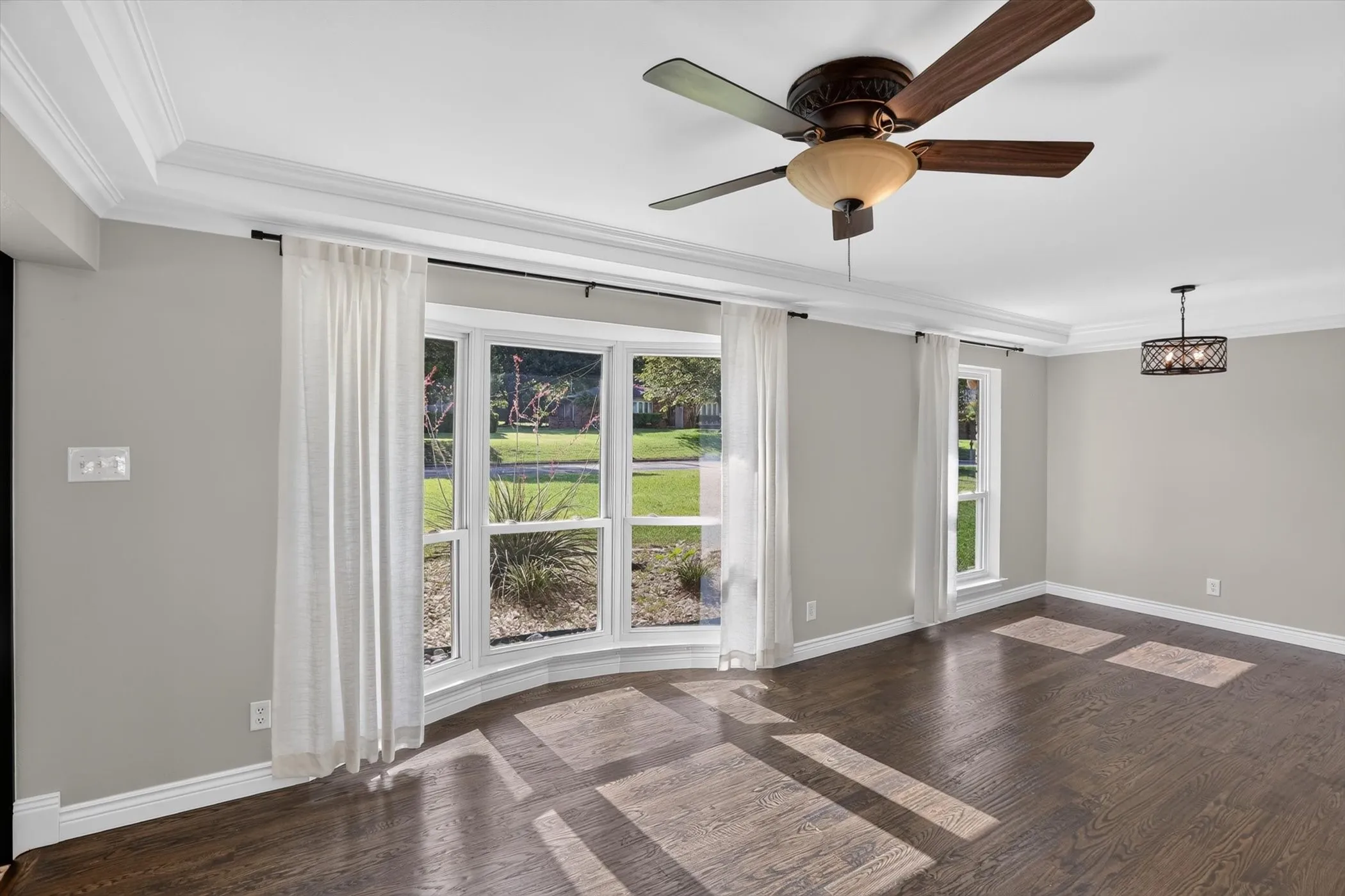 Bay window with multiple panes, wood-finish flooring, crown molding, ceiling fan, and decorative chandelier