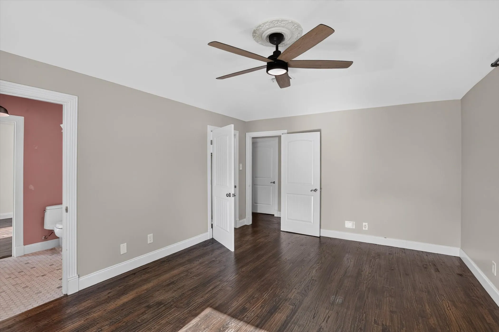 Spacious room featuring dark wood-finish flooring, light gray wall paint, and white trim