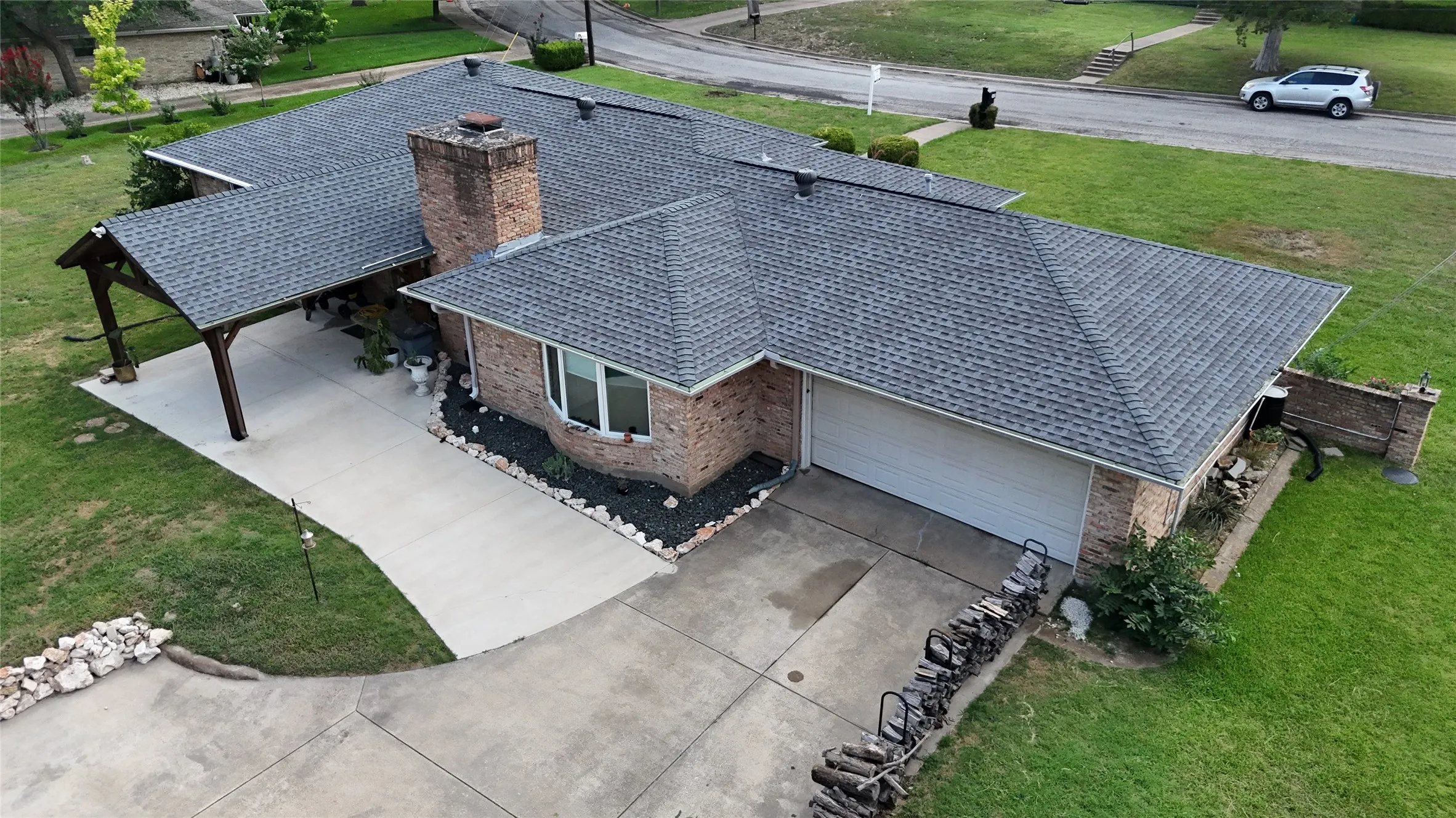 Brick residence featuring a charcoal shingle roof, attached two-car garage, and a covered carport