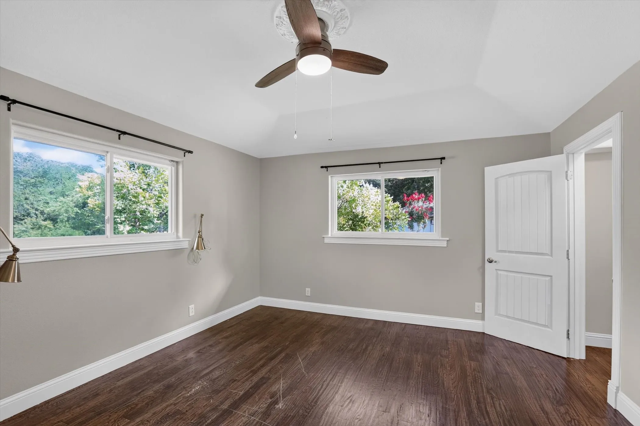 Vaulted ceiling with a decorative ceiling fan, wood-finish flooring, and two windows providing natural light