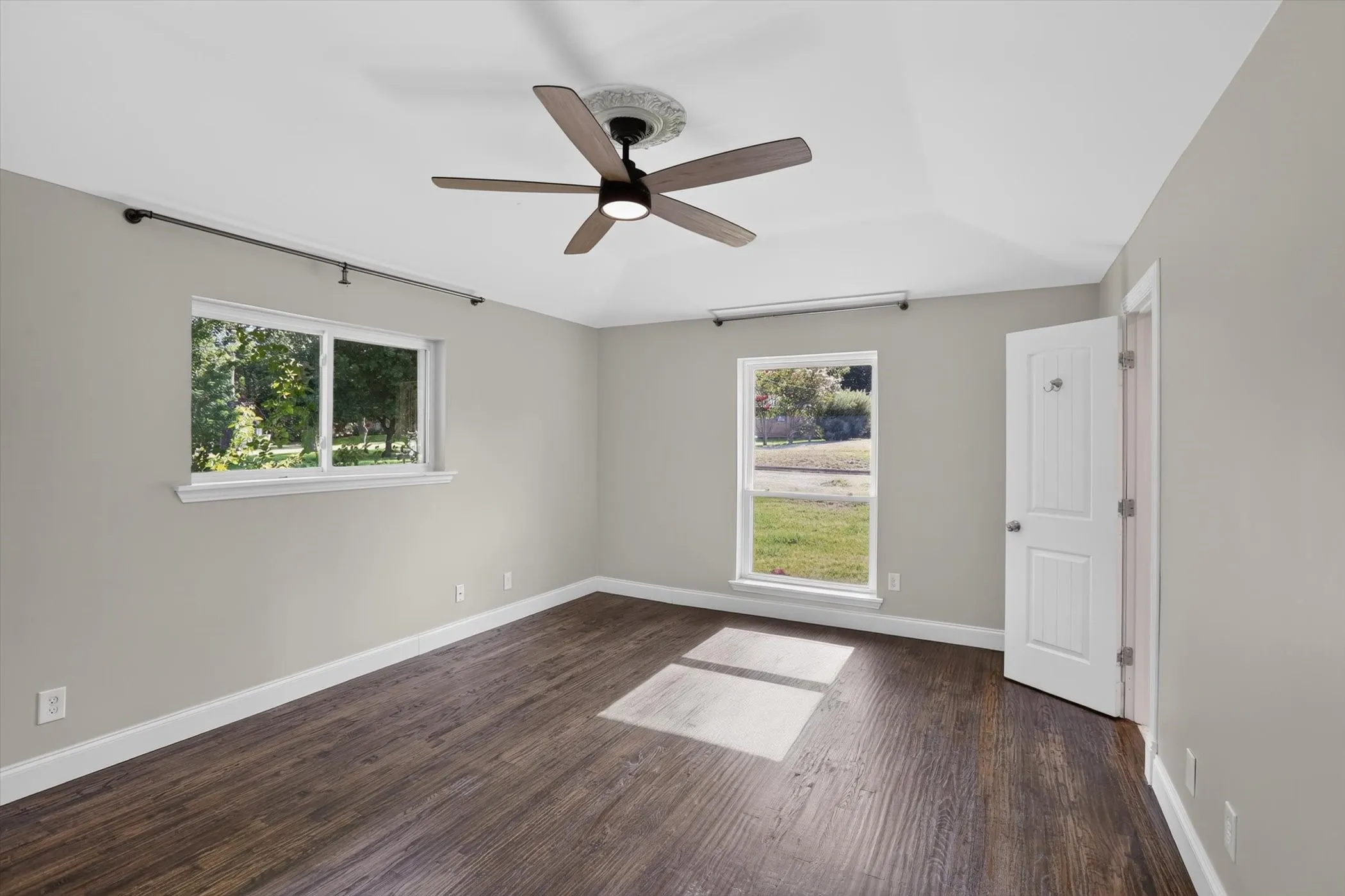 Spacious interior room with wood-finish flooring, two large windows, vaulted ceiling, and a ceiling fan with light fixture