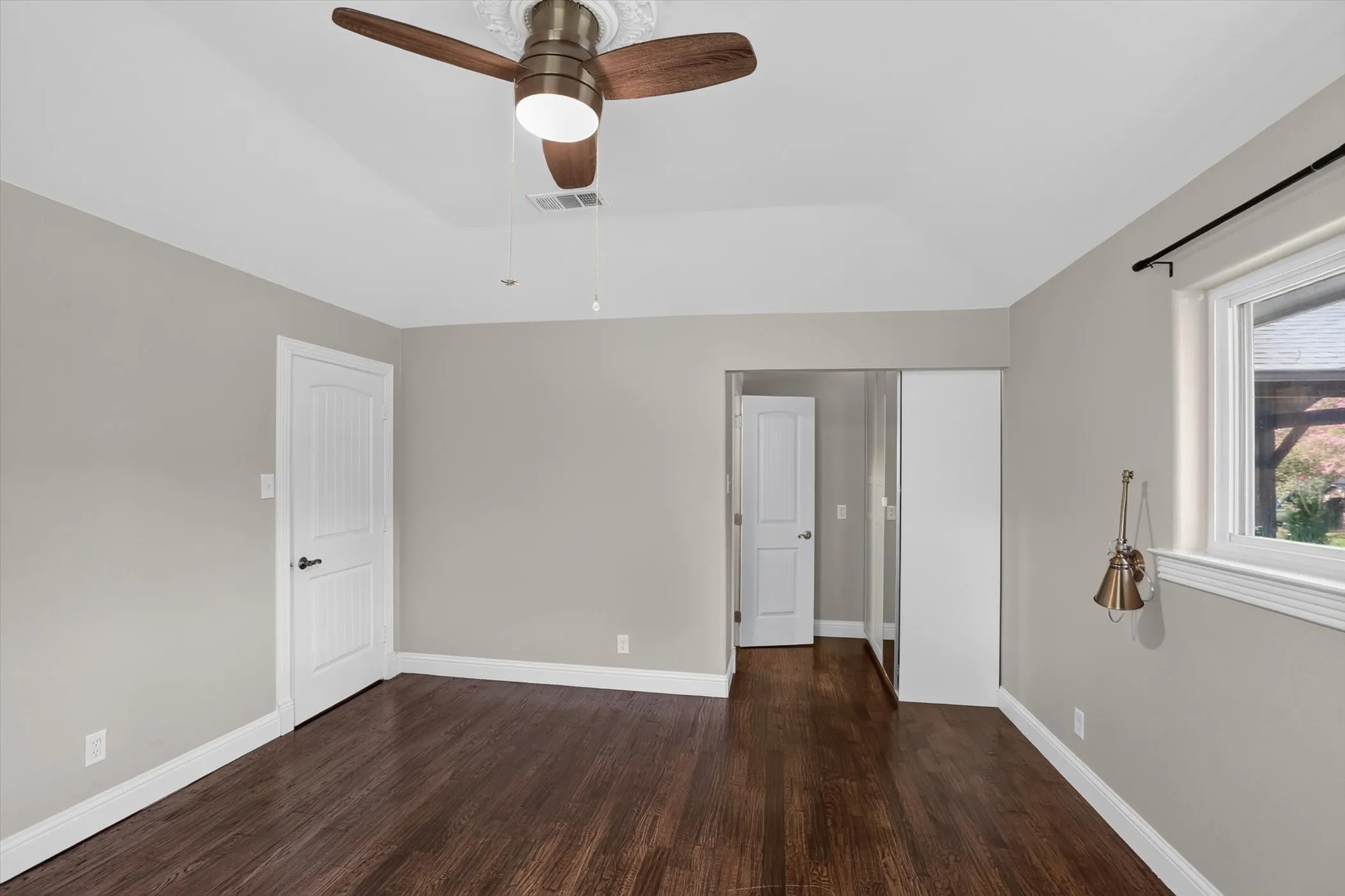 Spacious room featuring wood-finish flooring, light tan walls, and a vaulted ceiling with a built-in fan light fixture
