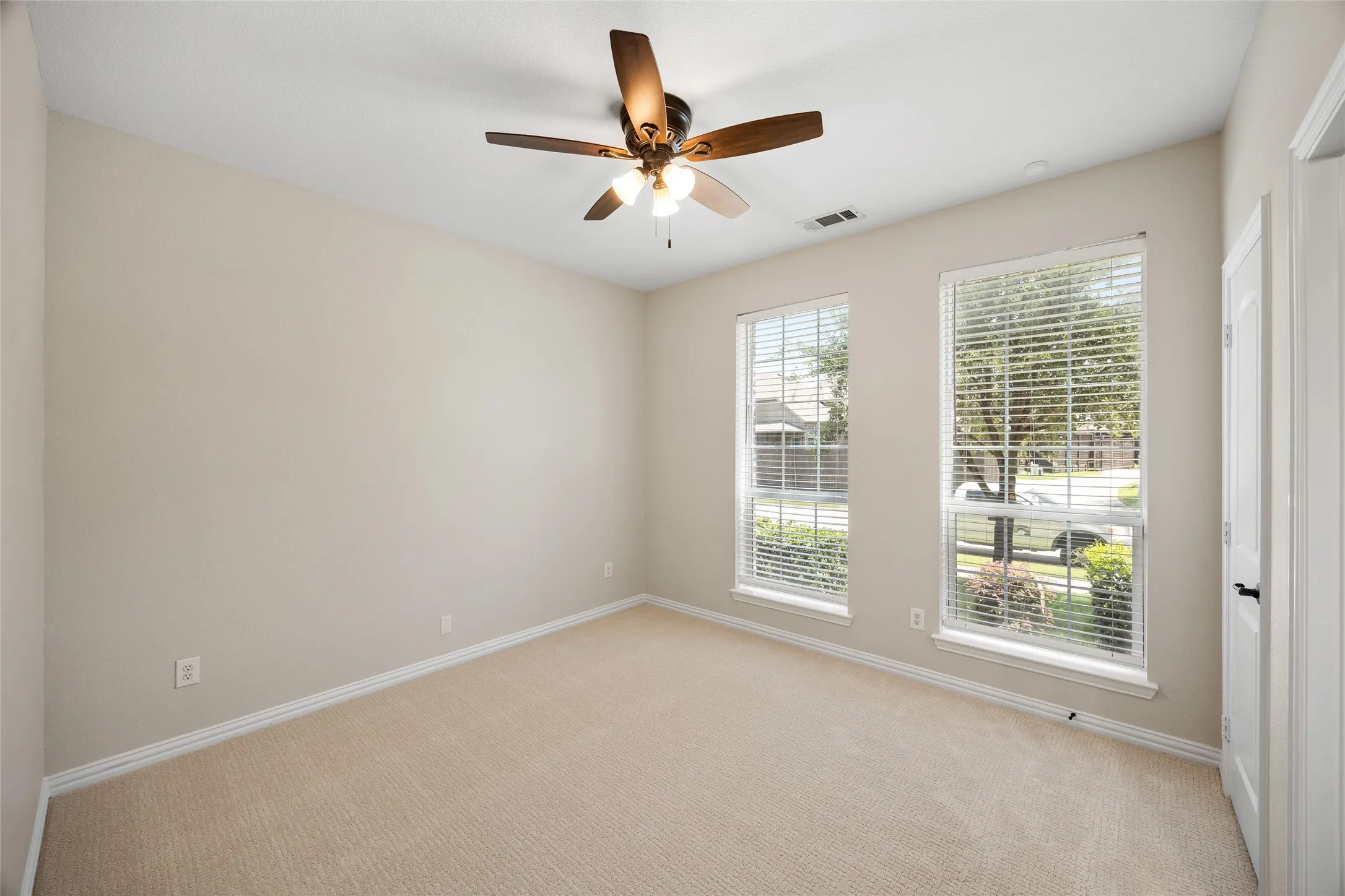 Carpeted room featuring two windows with horizontal blinds, a ceiling fan with light fixture, and neutral-toned walls