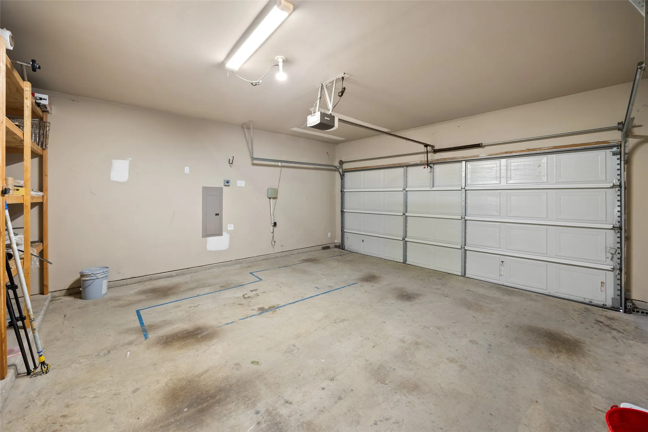 Spacious garage featuring a concrete floor, overhead fluorescent lighting, an automatic garage door opener, and built-in shelving