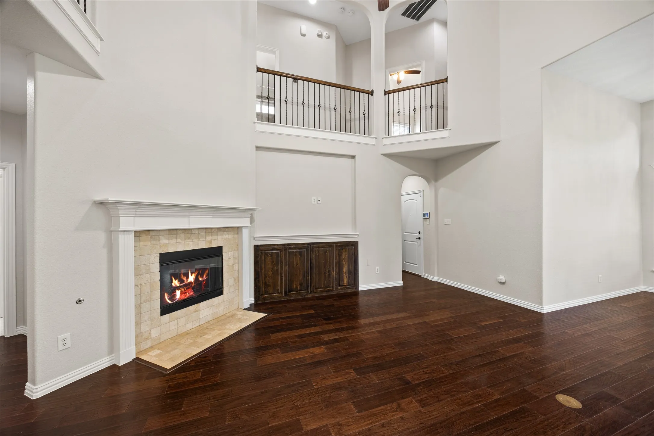 Two-story living area featuring dark wood-finish flooring and a fireplace with a light-toned tile surround and white mantel