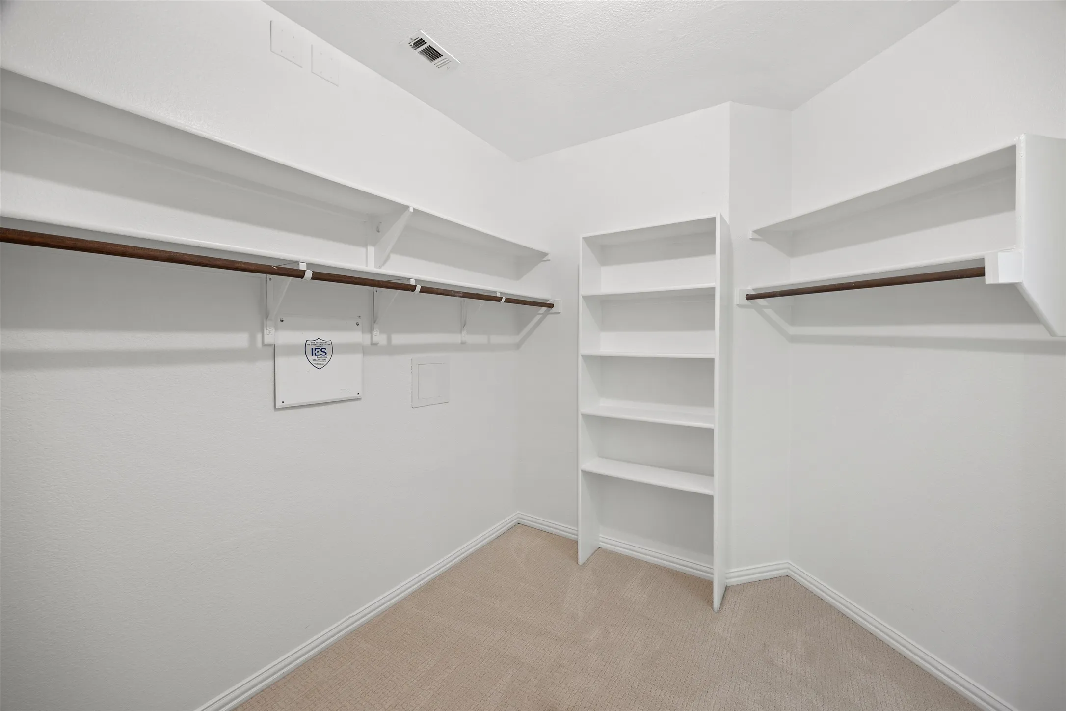 Walk-in closet with beige carpet flooring, multiple white shelving units, and two clothing rods