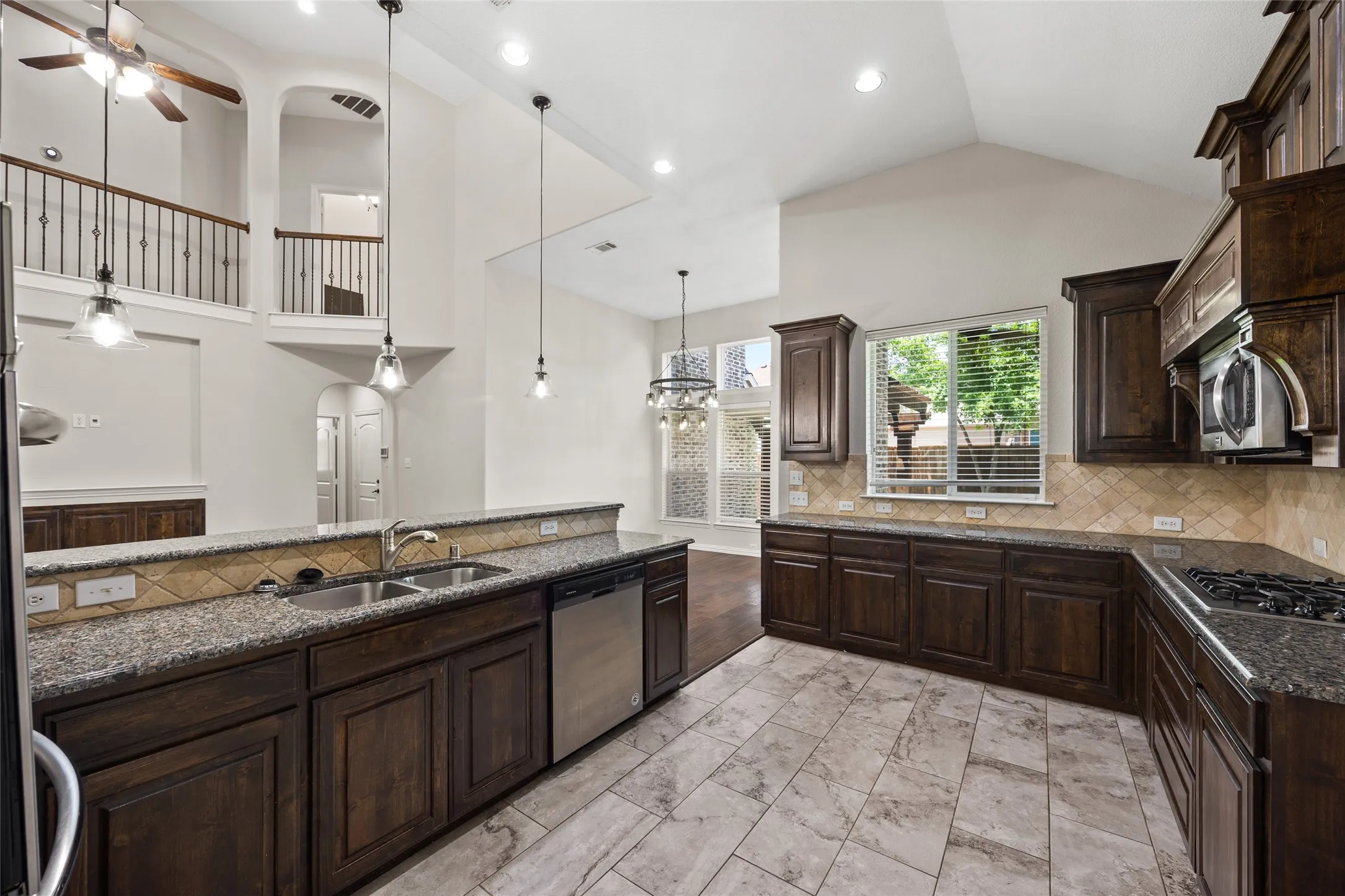 Spacious kitchen featuring dark wood cabinetry, stainless steel appliances, speckled countertops, and a neutral tile backsplash