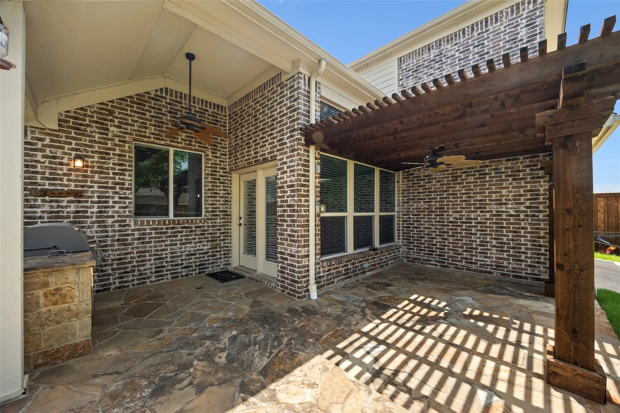Outdoor living space featuring a flagstone patio, a dark wood pergola, and a built-in outdoor grill station with stone cladding