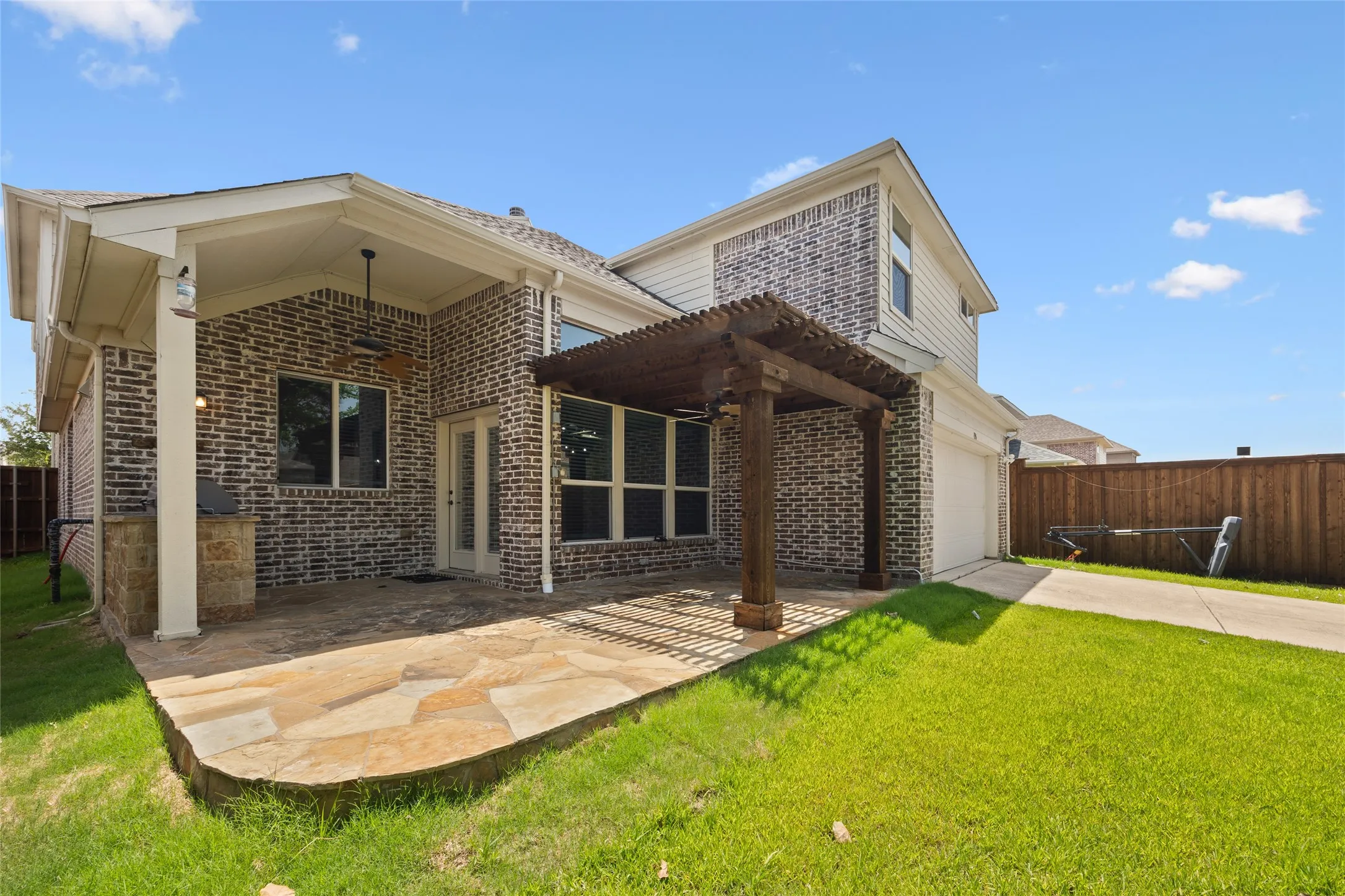 Expansive backyard featuring a natural stone patio, covered porch with ceiling fan, and a wood pergola