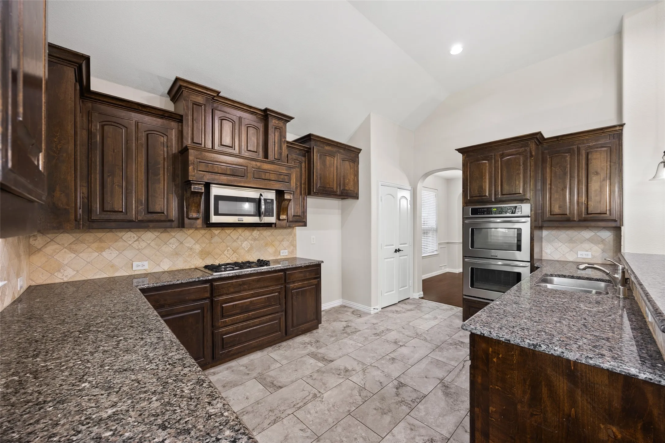 Spacious kitchen featuring dark wood cabinetry, granite-finish countertops, stainless steel appliances, and a diagonal tile backsplash
