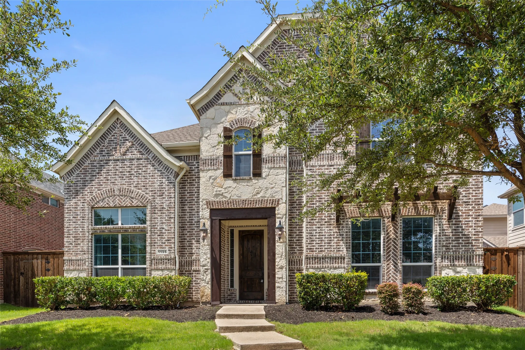 Two-story residence featuring a brick and stone facade with dark wood shutters