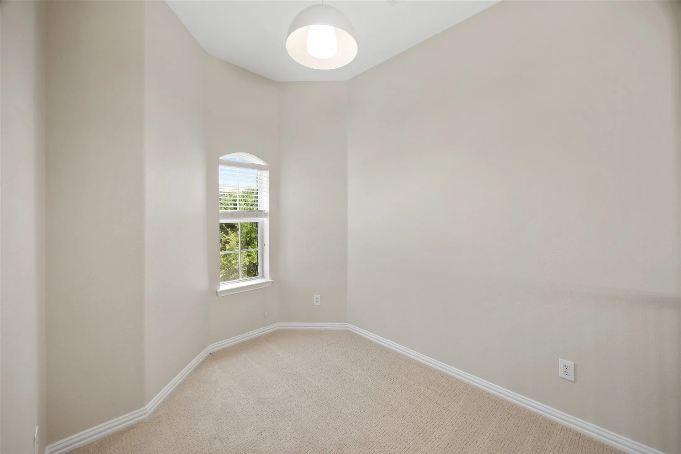Neutral-toned carpeted interior space with an arched window featuring blinds