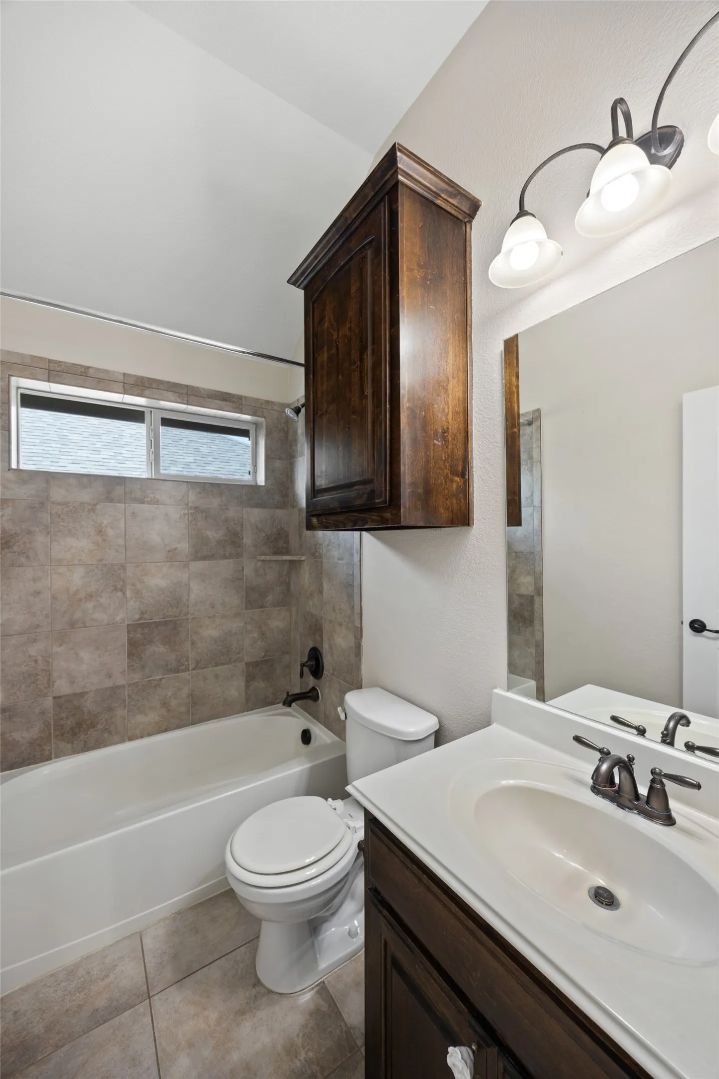 Bathroom featuring a white bathtub, ceramic tile shower surround, dark wood-finish vanity, white countertop, and integrated sink