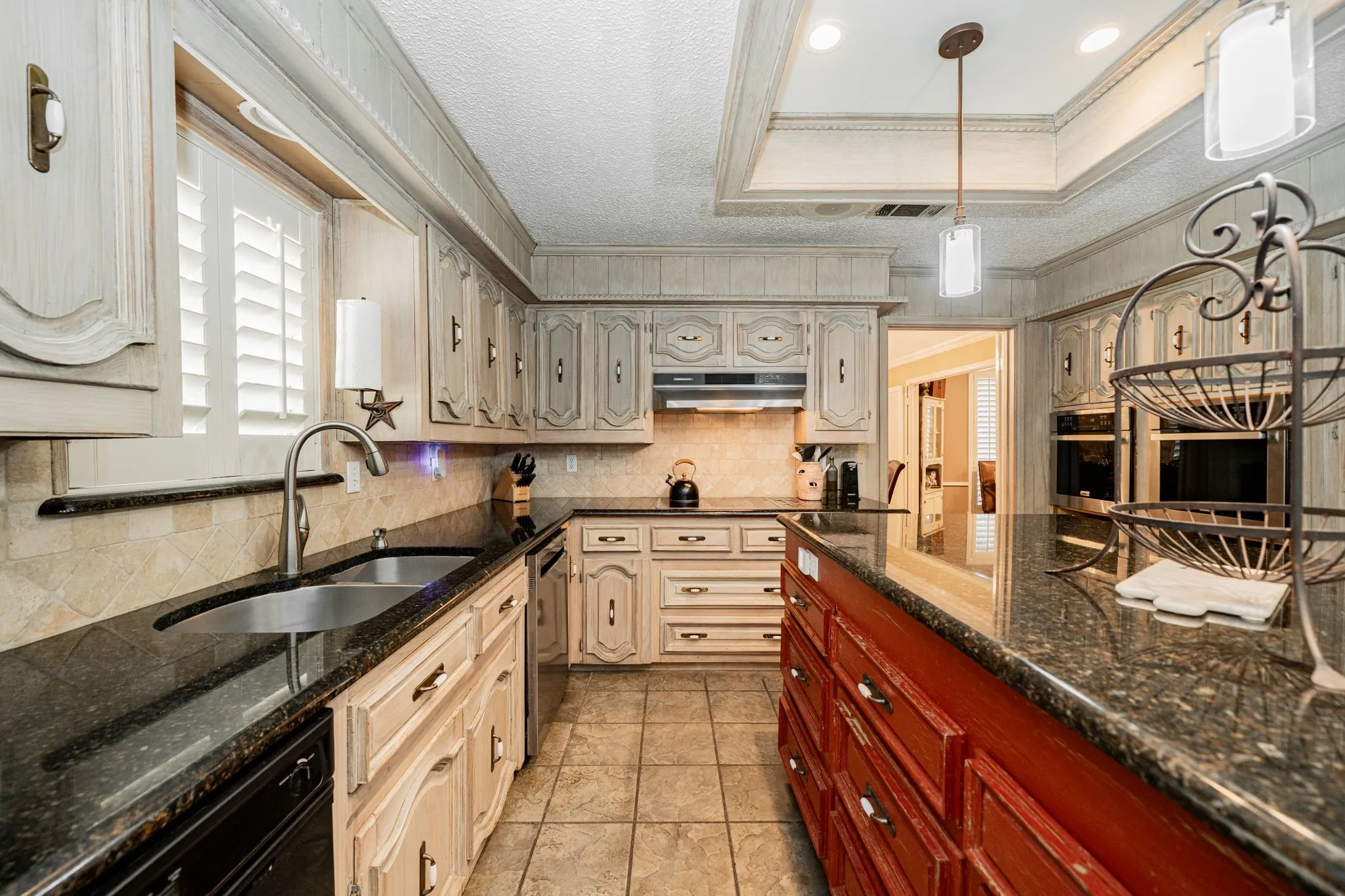 Kitchen with a raised ceiling, decorative backsplash, dark stone counters, decorative light fixtures, and healthy amount of natural light