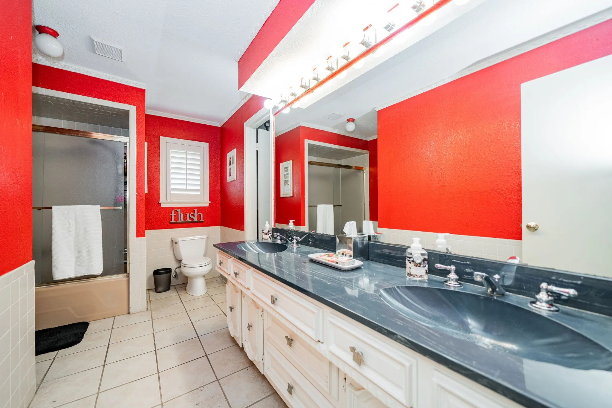 Full bathroom with double vanity, light tile patterned floors, combined bath / shower with glass door, tile walls, and a wainscoted wall
