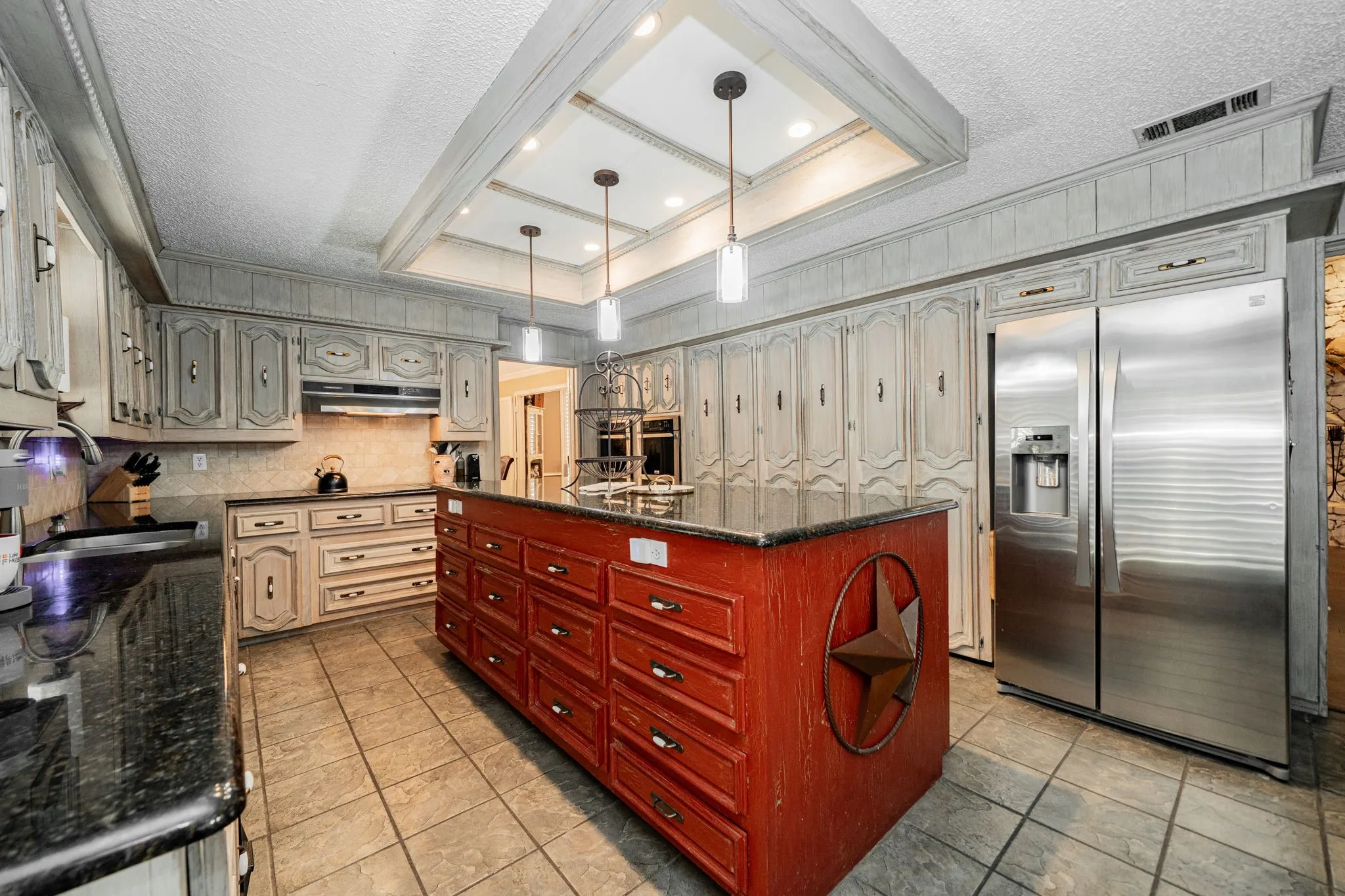 Kitchen with a raised ceiling, stainless steel appliances, a textured ceiling, dark stone counters, and decorative light fixtures