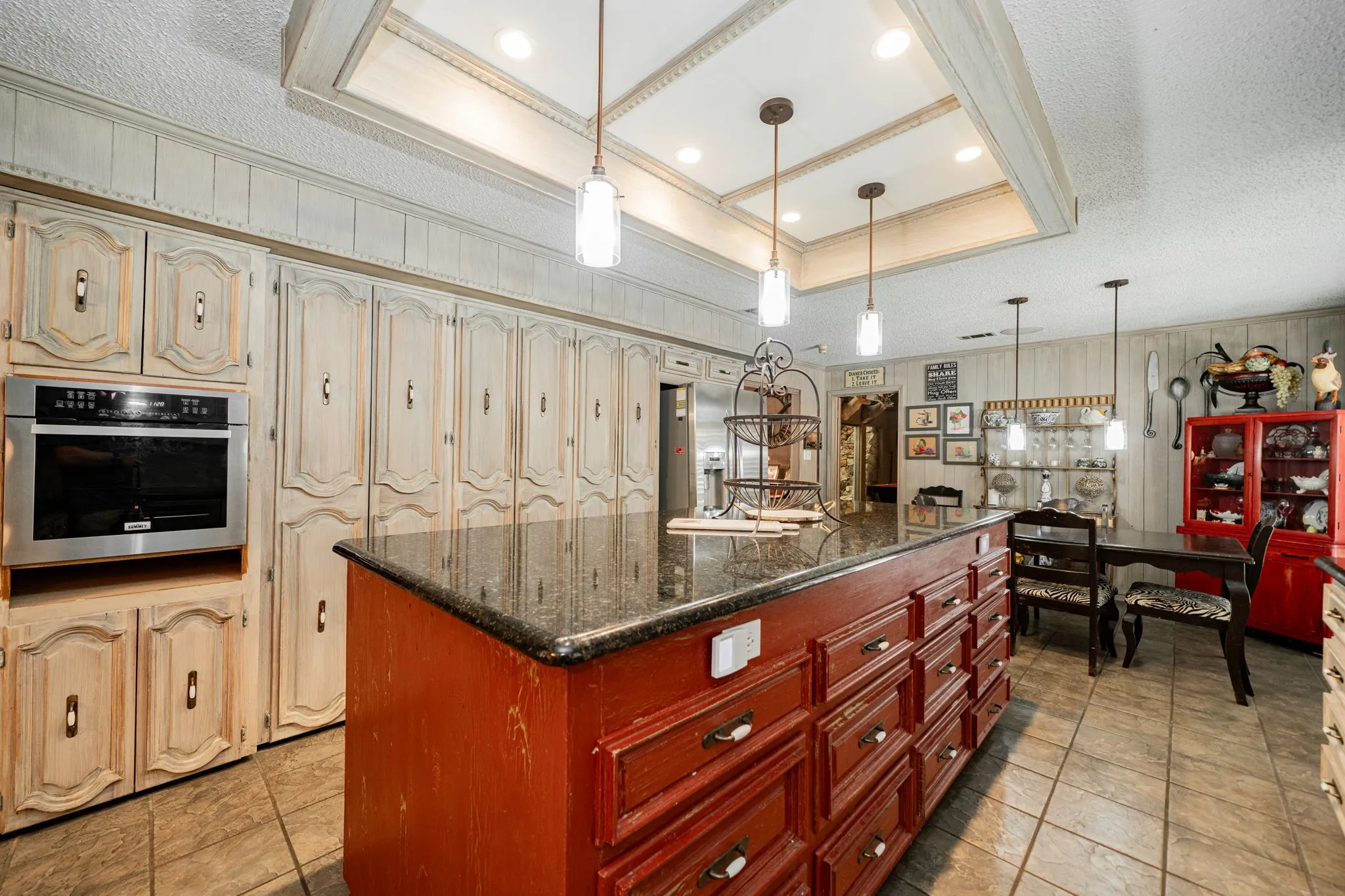 Kitchen with a raised ceiling, decorative light fixtures, dark stone countertops, oven, and a center island