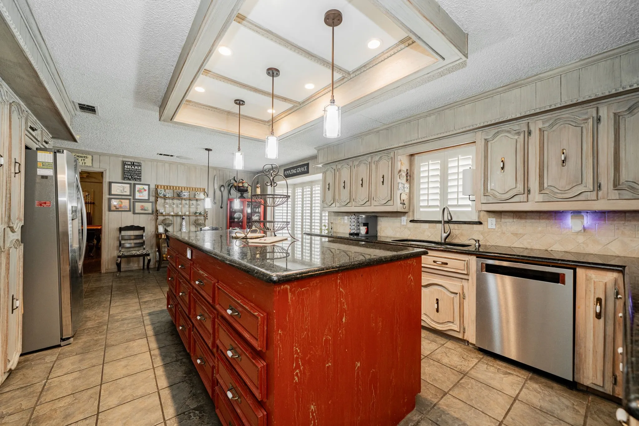 Kitchen featuring a raised ceiling, a textured ceiling, a kitchen island, appliances with stainless steel finishes, and dark stone counters