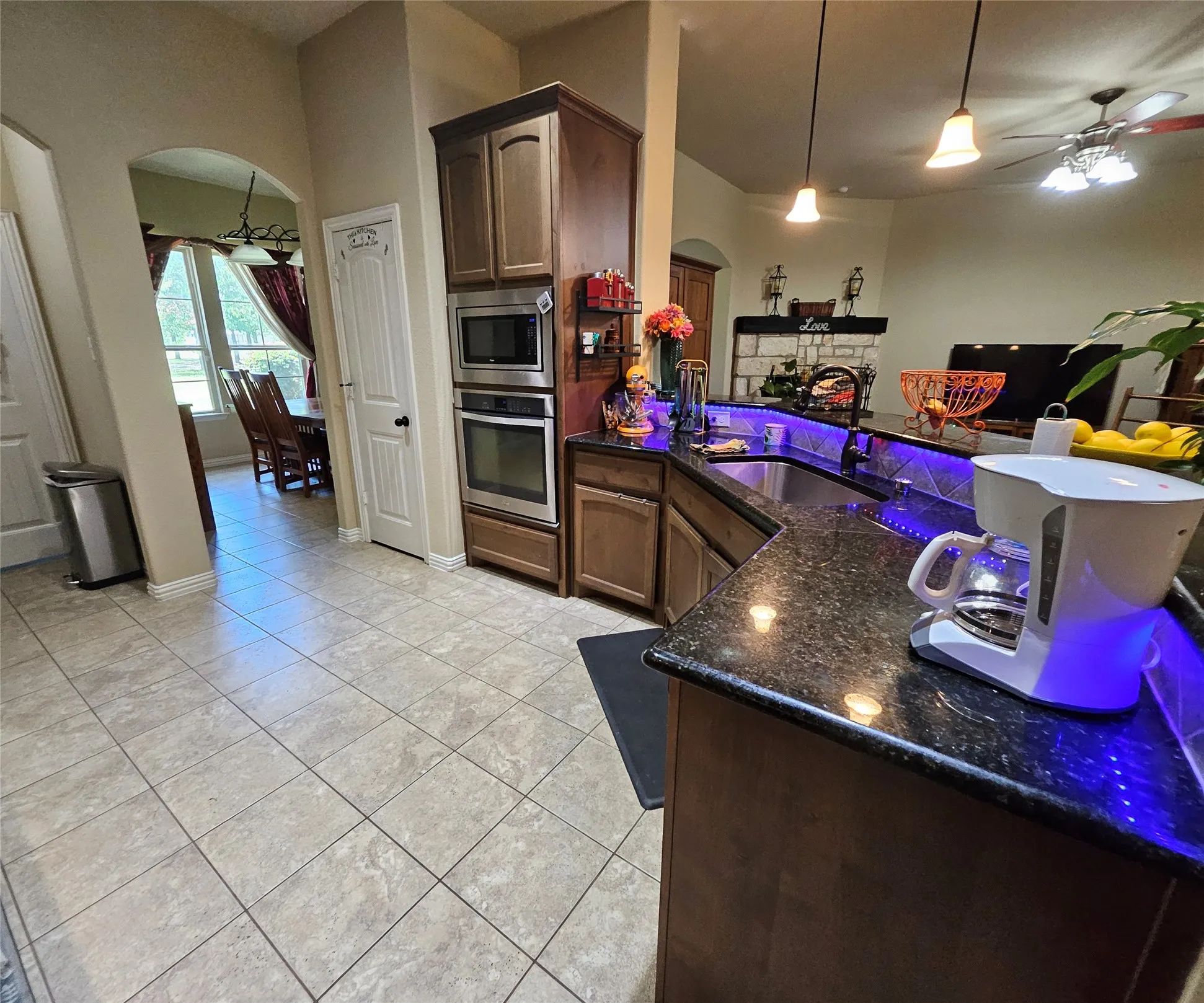Kitchen featuring a built-in stainless steel microwave and oven, dark wood cabinetry, granite countertops, and tile flooring