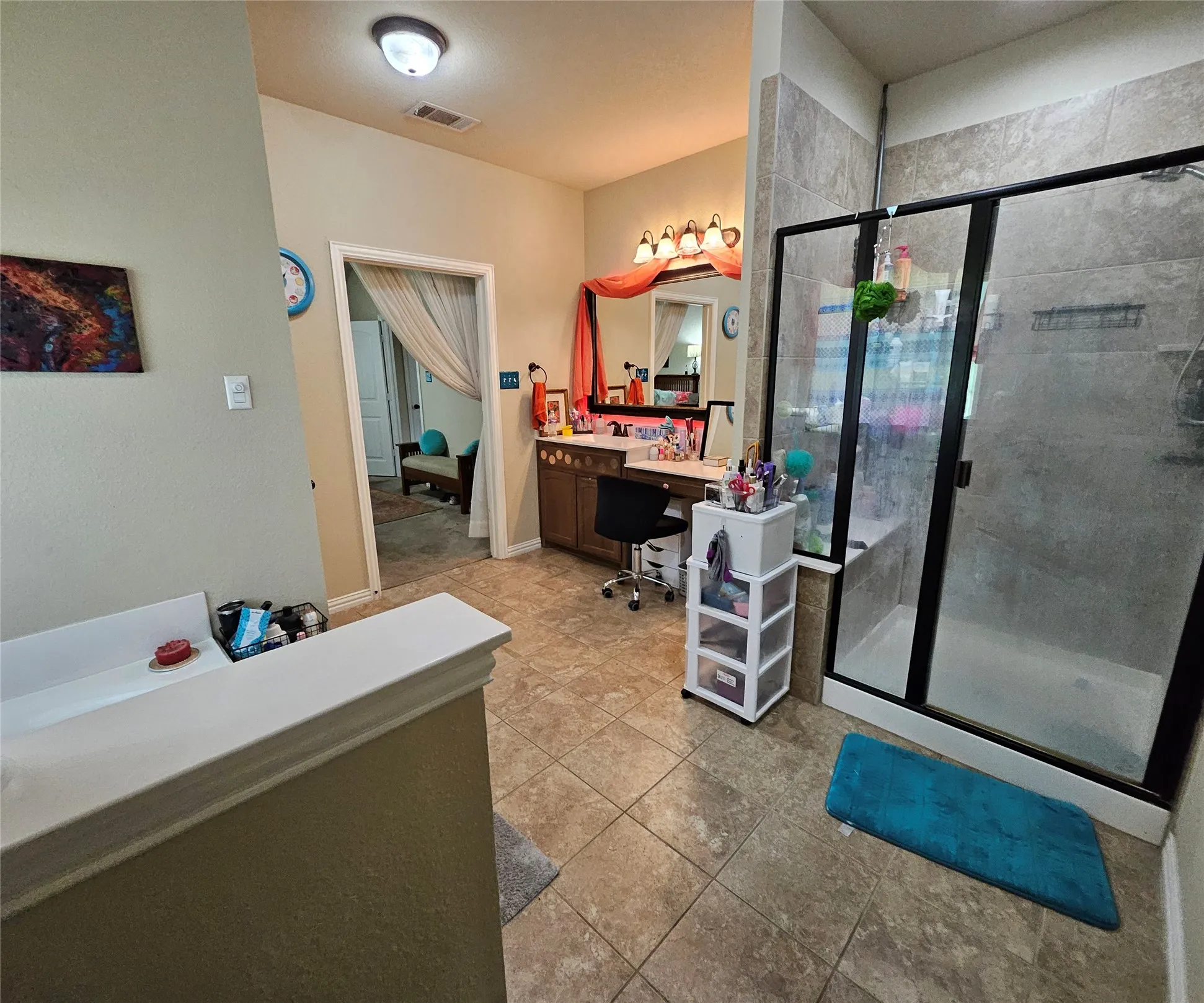 Spacious bathroom featuring a glass-enclosed shower, a wood-finish vanity with a built-in makeup area, and tile flooring