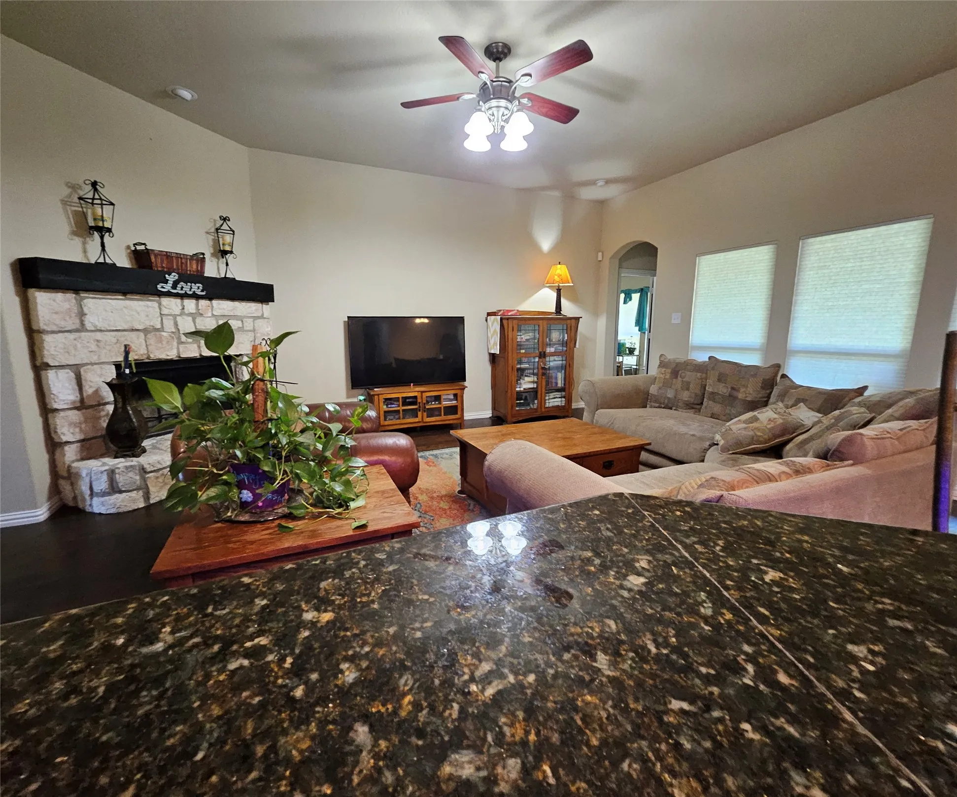 Spacious living area featuring a stone-clad fireplace with a dark wood mantel, vaulted ceiling, and dark wood-finish flooring