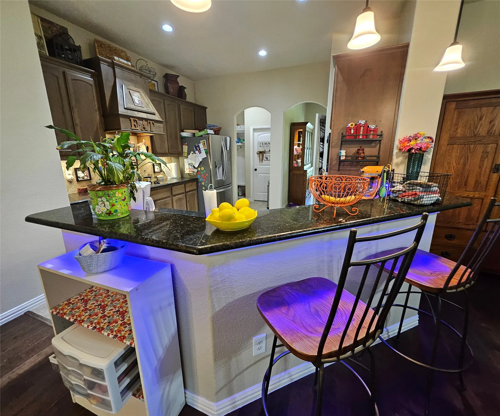Kitchen featuring an eat-at peninsula with dark granite countertops, recessed lighting, and dark wood-finish cabinetry