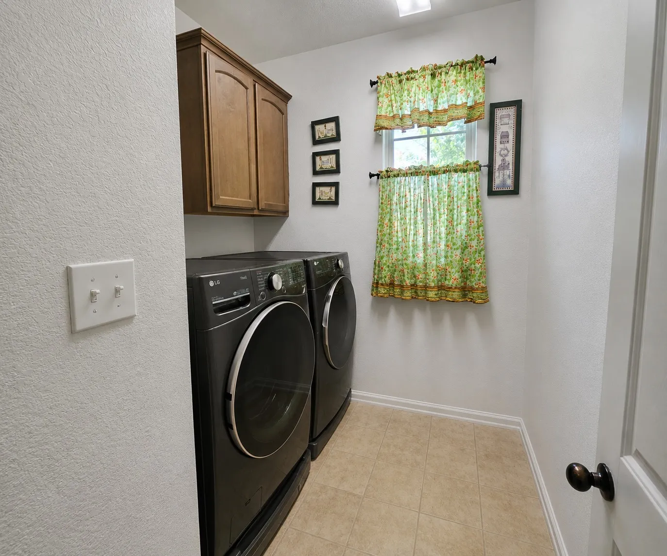 Laundry room featuring wood-finish cabinetry, light-toned tile flooring, and a window for natural light