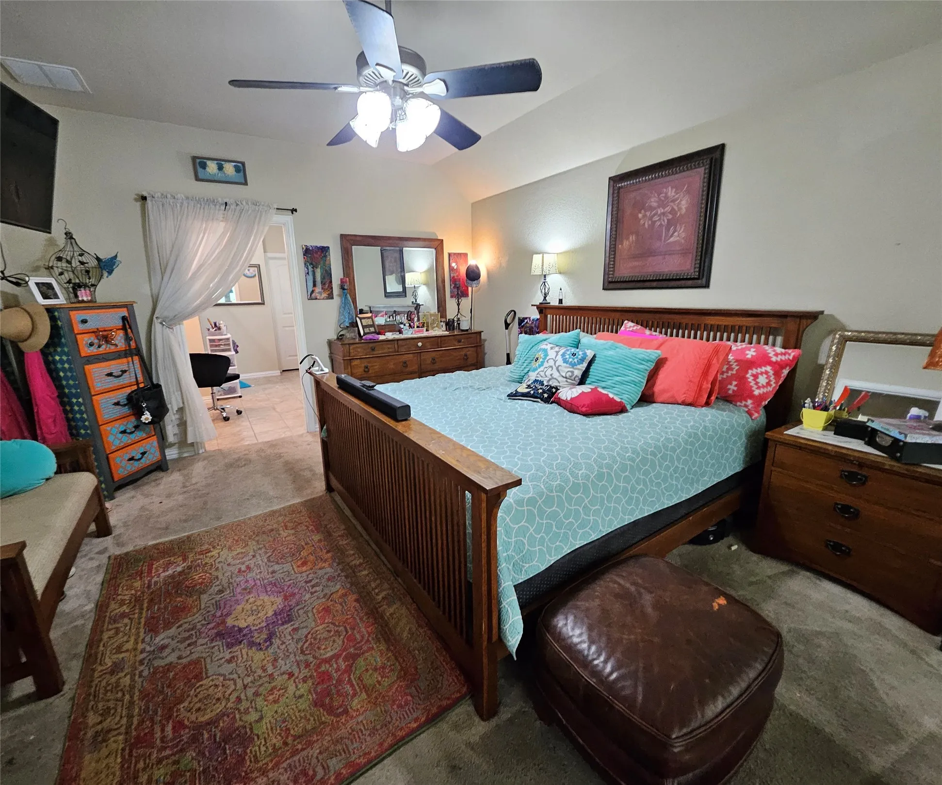 Vaulted ceiling with a ceiling fan, carpeted flooring, and an adjoining space with tile flooring