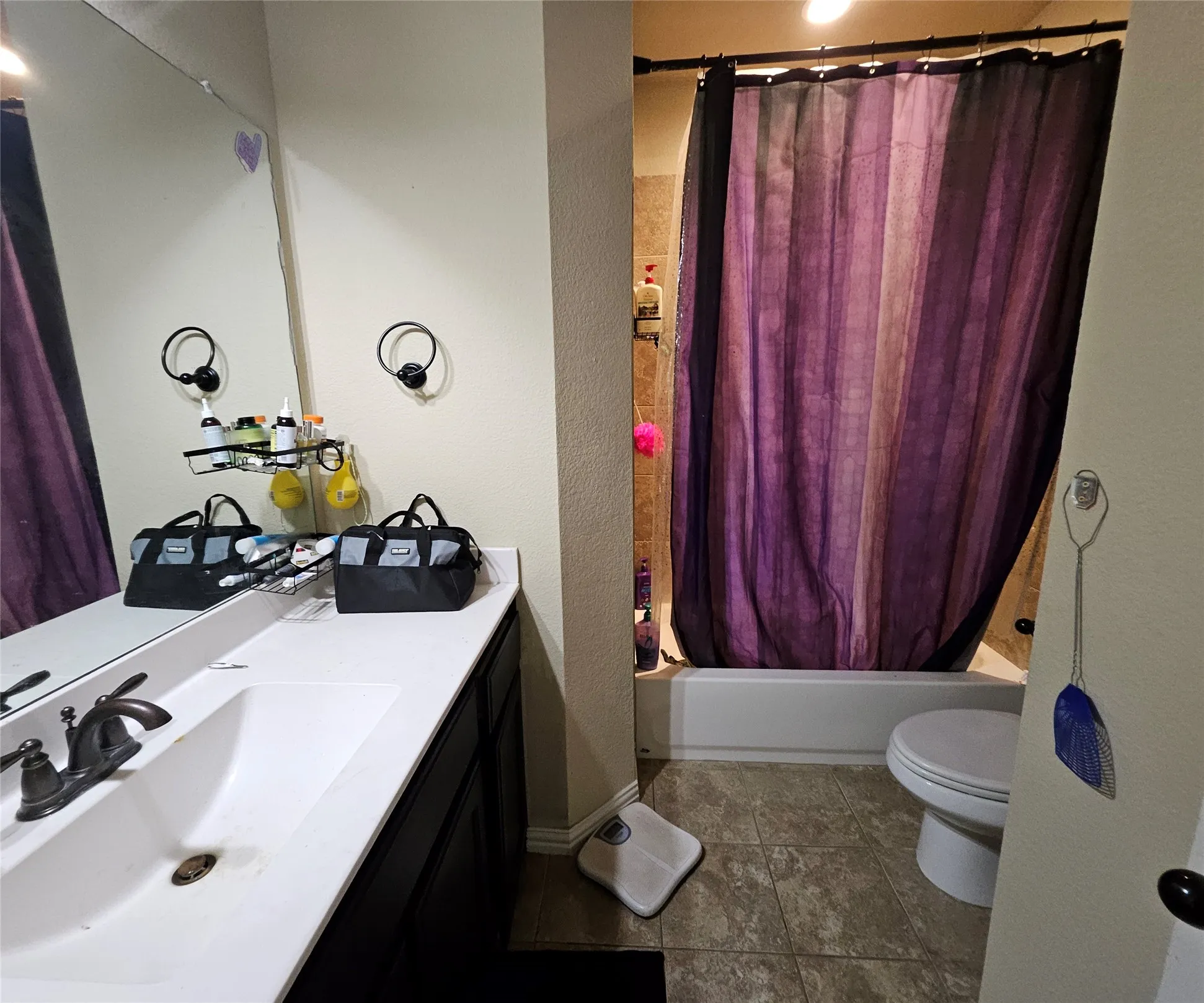 Bathroom featuring a single vanity with a white countertop and dark cabinetry, a large wall-mounted mirror, a tub and shower combination with light-colored tile surround, and tiled flooring