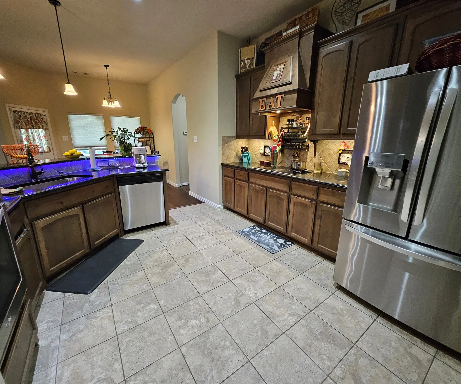 Kitchen featuring tile flooring, dark wood cabinetry, a built-in stainless steel dishwasher, stainless steel refrigerator, and pendant lighting