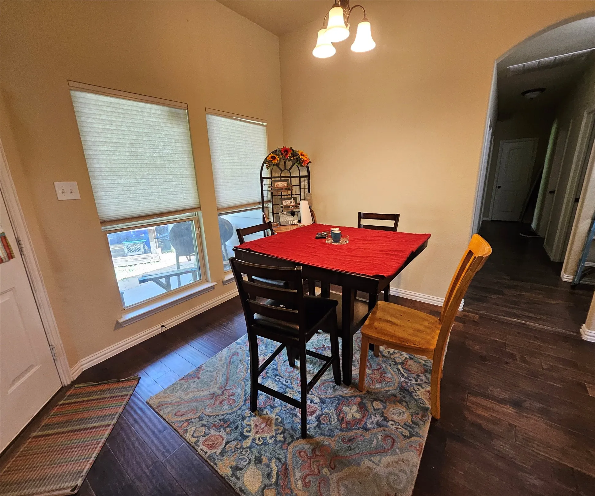 Dining area featuring wood-finish flooring, two windows with cellular blinds, a ceiling-mounted light fixture, and an arched entryway