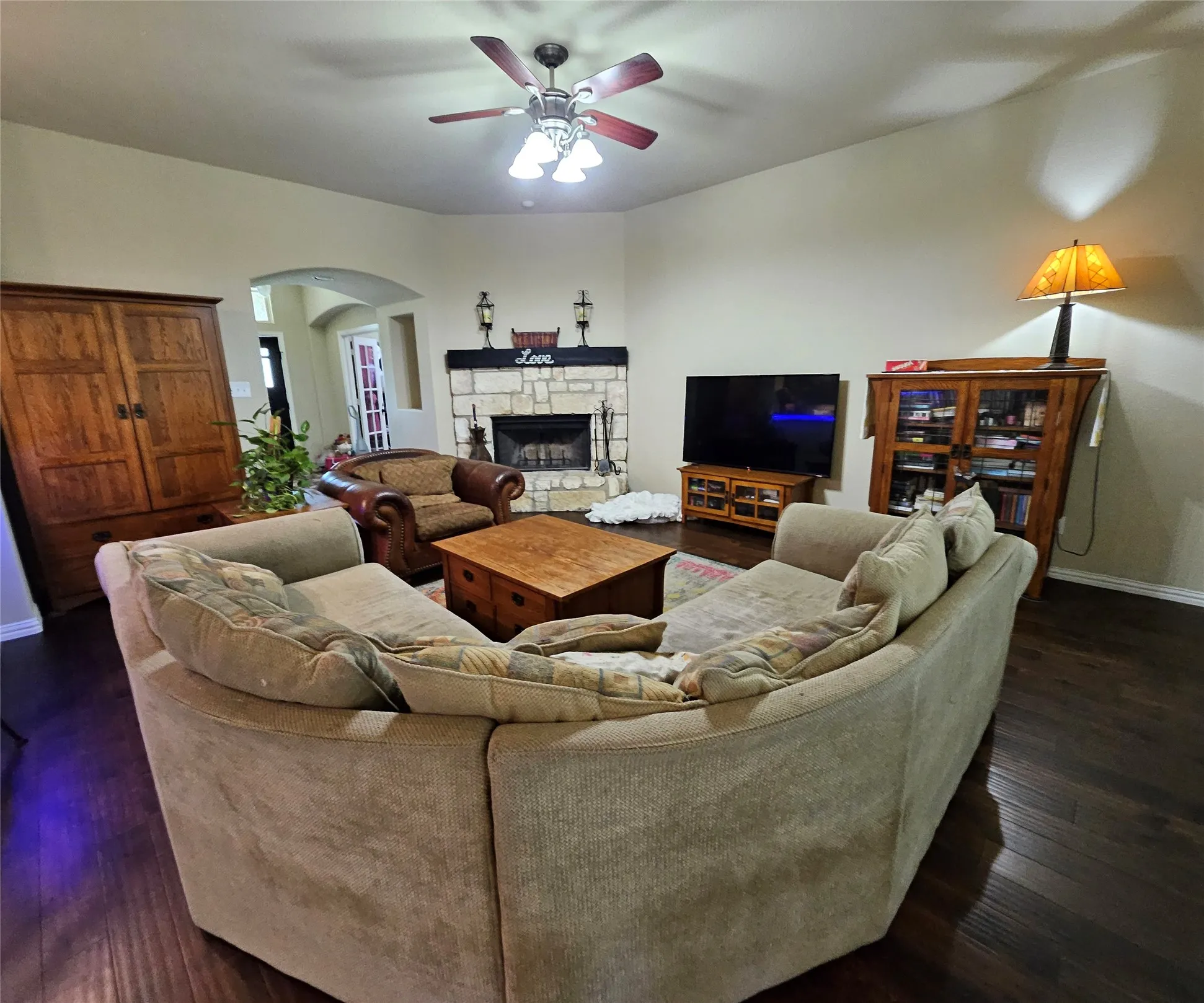 Living area featuring rich wood-finish flooring, a stone fireplace with a dark wood mantel, and an arched entryway