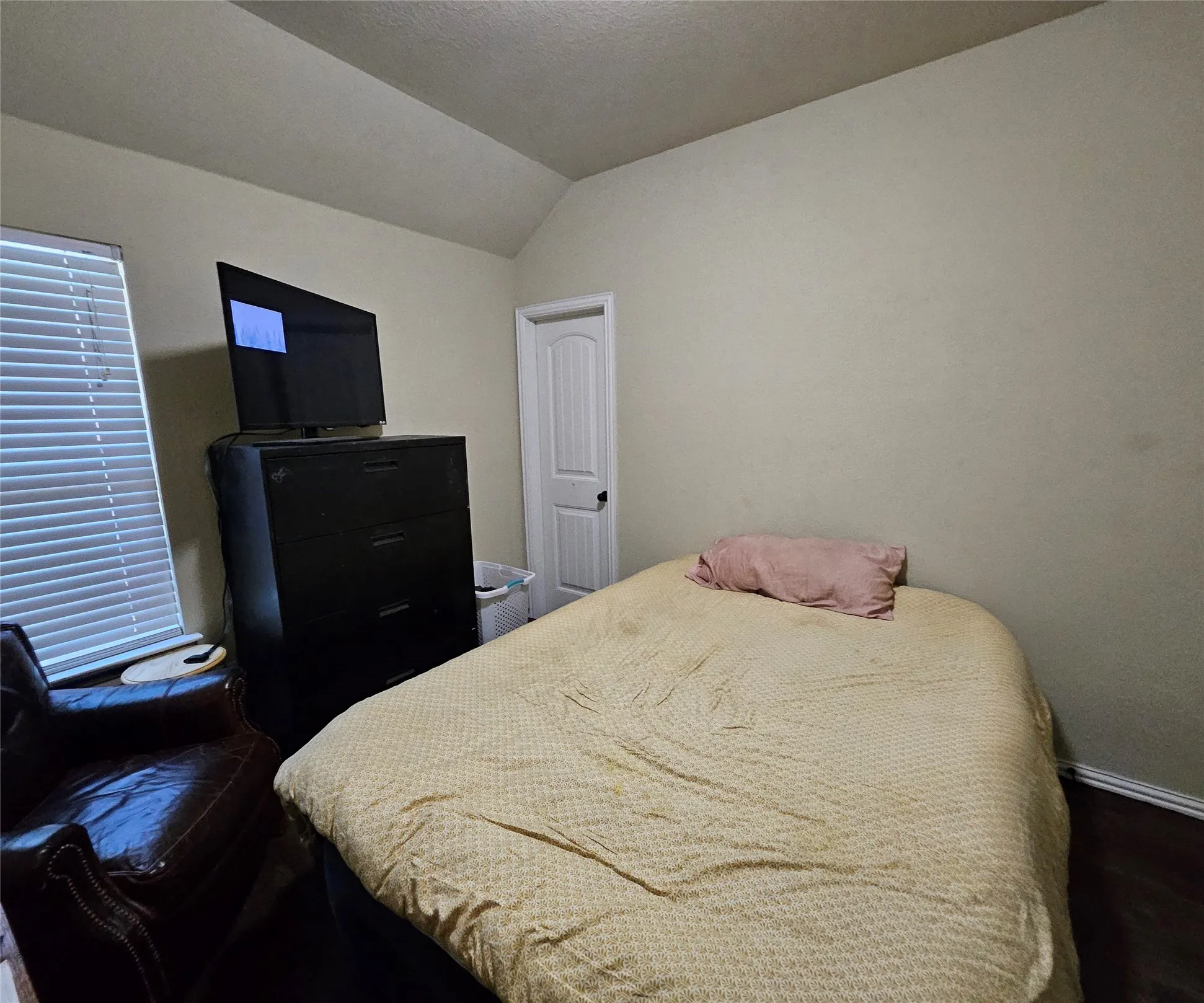 Room featuring an angled ceiling, wood-finish flooring, and a white interior door with a black handle
