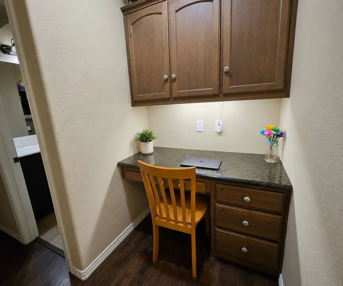 Built-in desk area featuring a dark stone-finish countertop, wood-finish cabinetry, and under-cabinet lighting