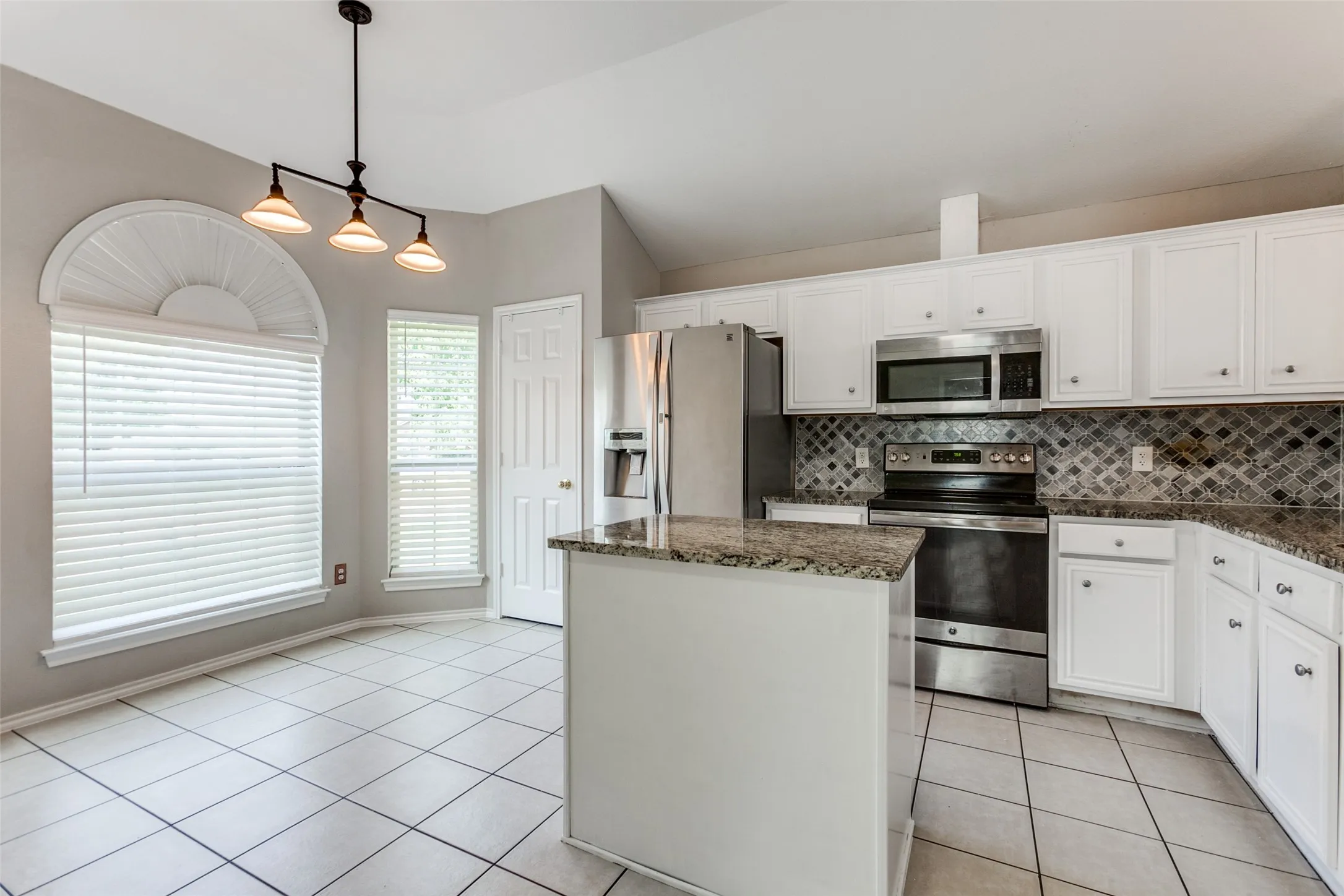 Kitchen featuring white cabinetry, granite countertops, stainless steel appliances, a decorative tile backsplash, and tile flooring