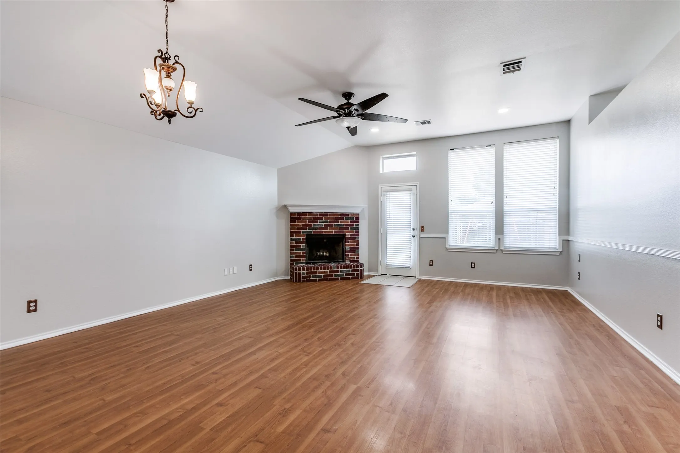 Spacious room featuring wood-finish flooring, a brick fireplace with mantel, a vaulted ceiling with a ceiling fan, and multiple windows