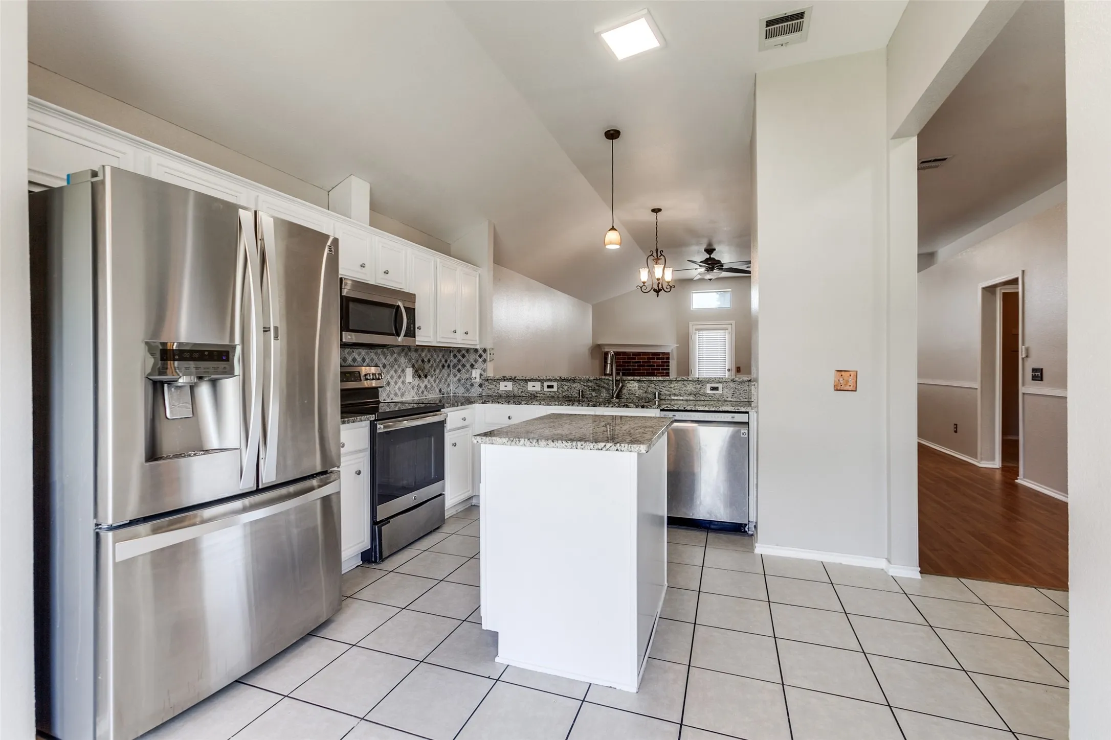 Modern kitchen featuring stainless steel appliances, white cabinetry, granite countertops, and a tile backsplash