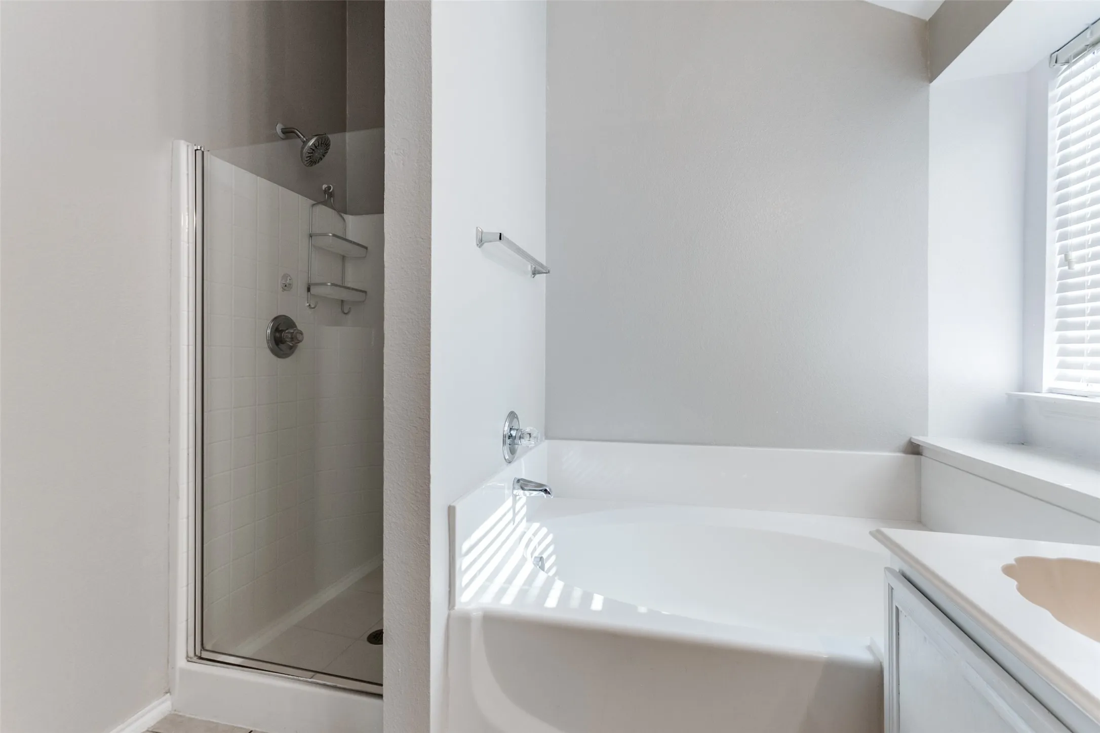 Bathroom featuring an enclosed shower with white tiled walls, a separate bathtub, a window with blinds, and a vanity with an integrated sink