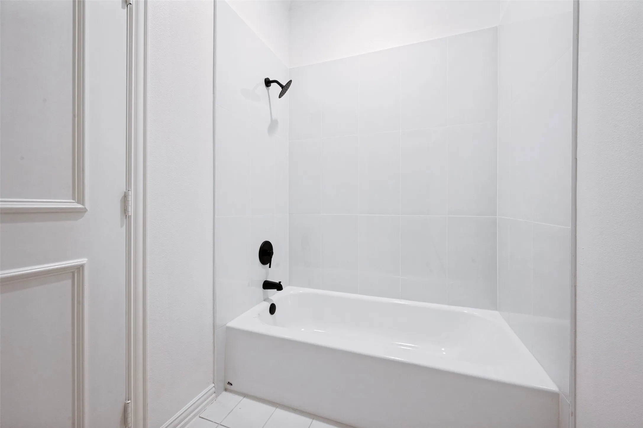 White bathtub with matte black fixtures, white subway tile surround, and coordinating white floor tiles