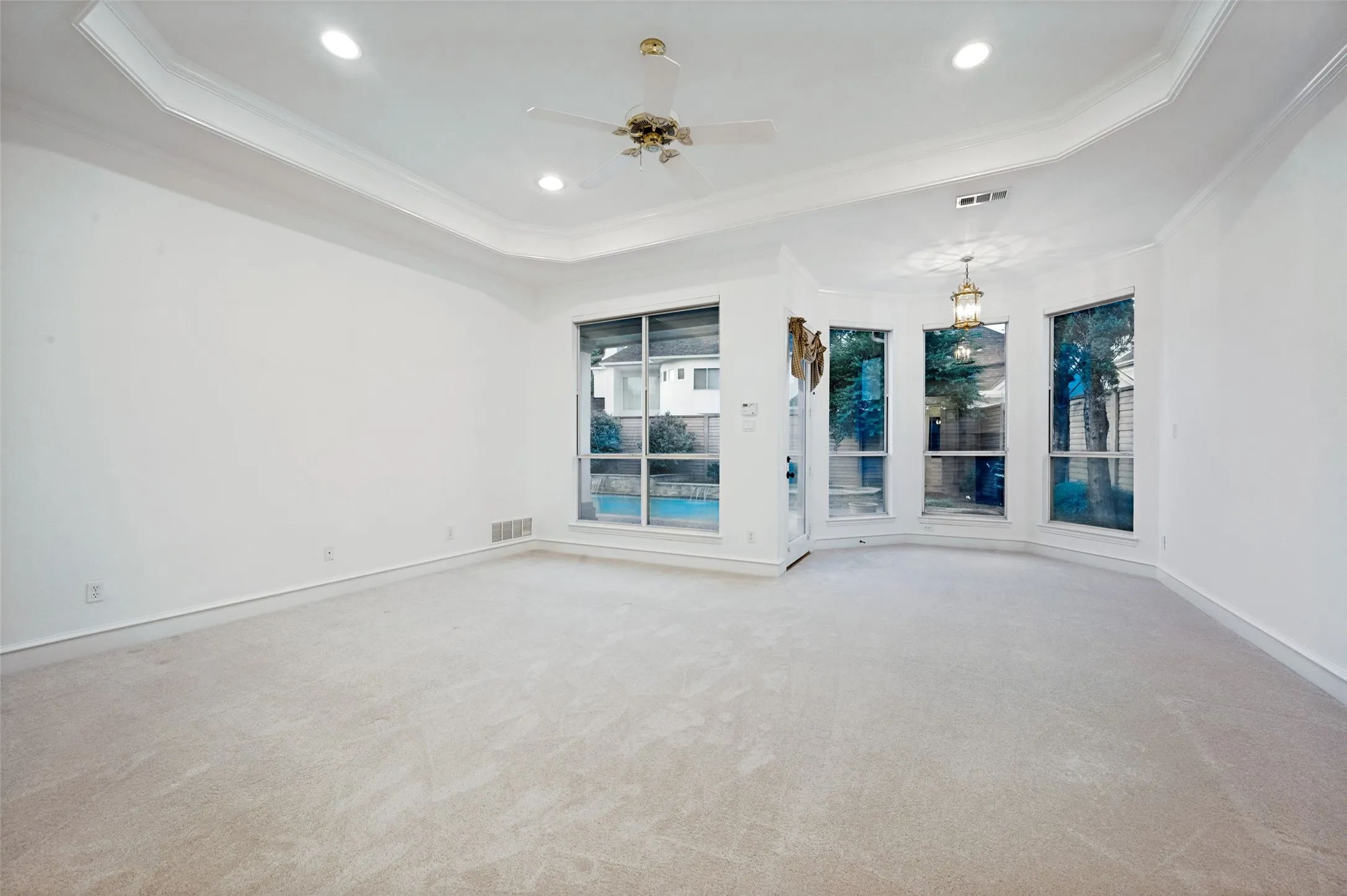 Spacious room featuring multiple large windows, recessed lighting, a ceiling fan, crown molding, and light-toned carpet flooring
